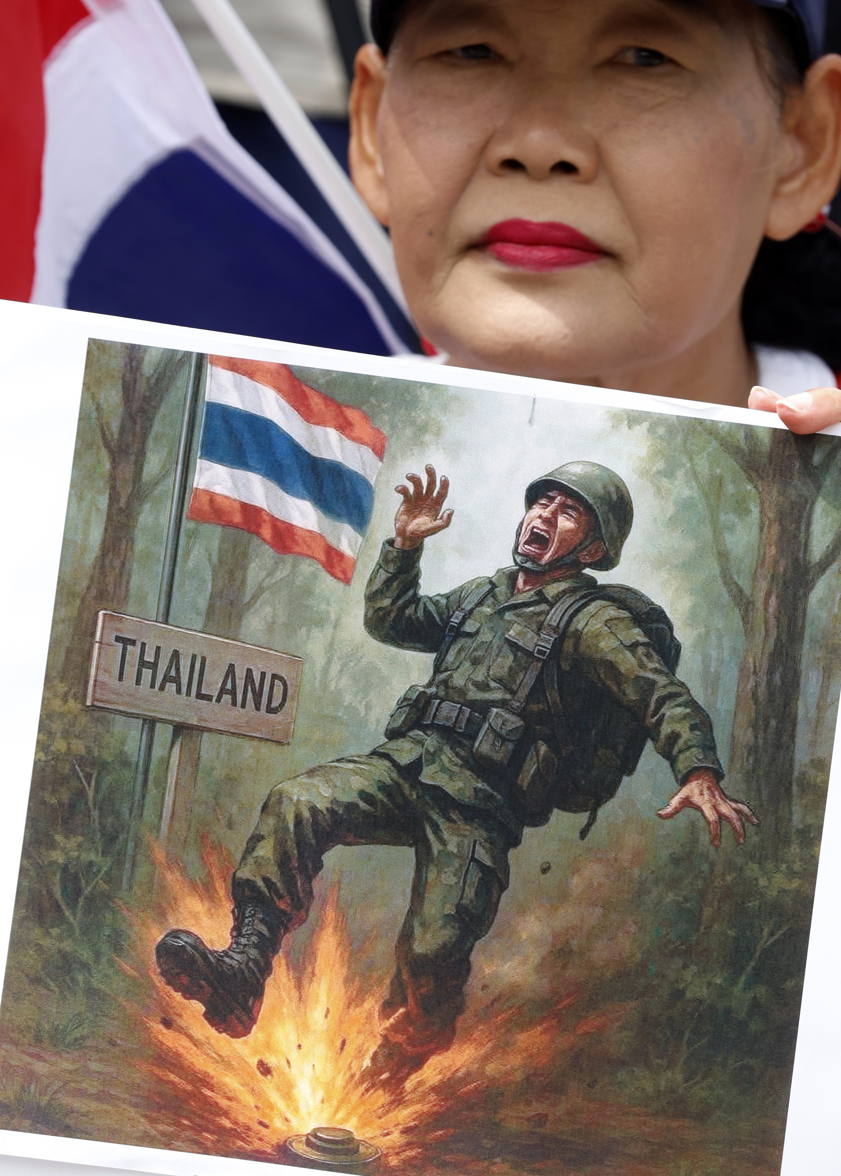 An sign depicting a soldier being hit by a landmine is held up by a Thai woman during a protest rally in Bangkok on Sunday. Photo: EPA