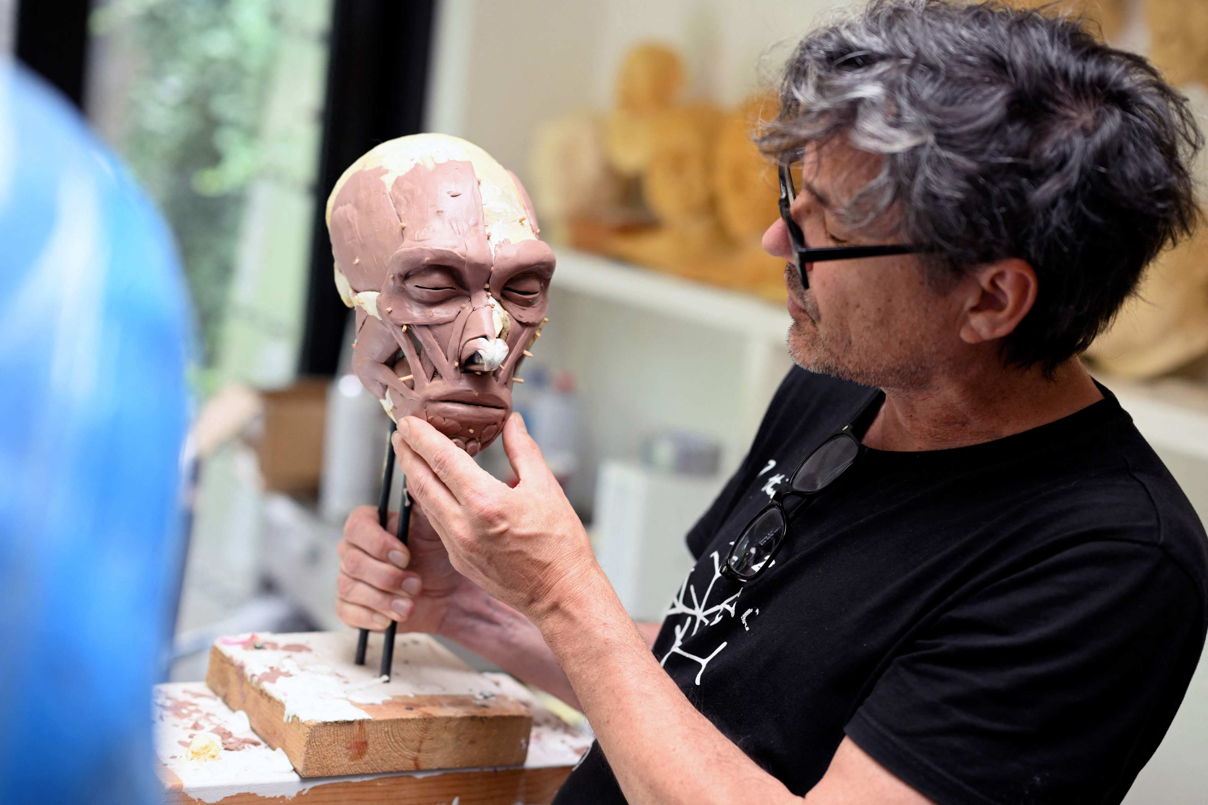 Dutch artist Alfons Kennis holds a model under construction representing a prehistoric human skull in his workshop in Arnhem, on July 3, 2025. Alfons and his twin brother Adrie are known for their paleo-anthropological work. Photo: AFP