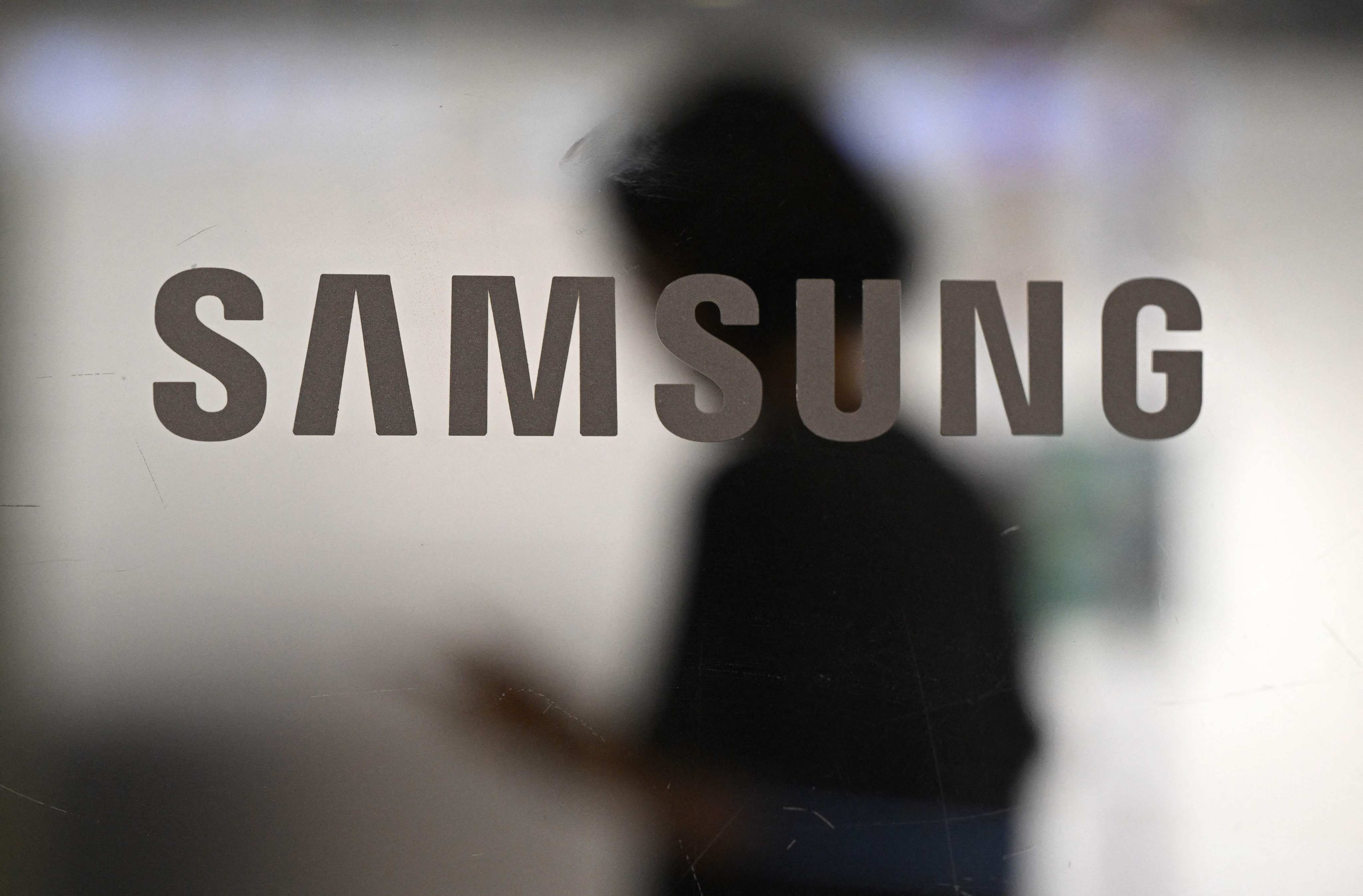 A woman walks past a logo of Samsung Electronics displayed on a glass door at the company’s Seocho building in Seoul on July 8, 2025. Photo: AFP