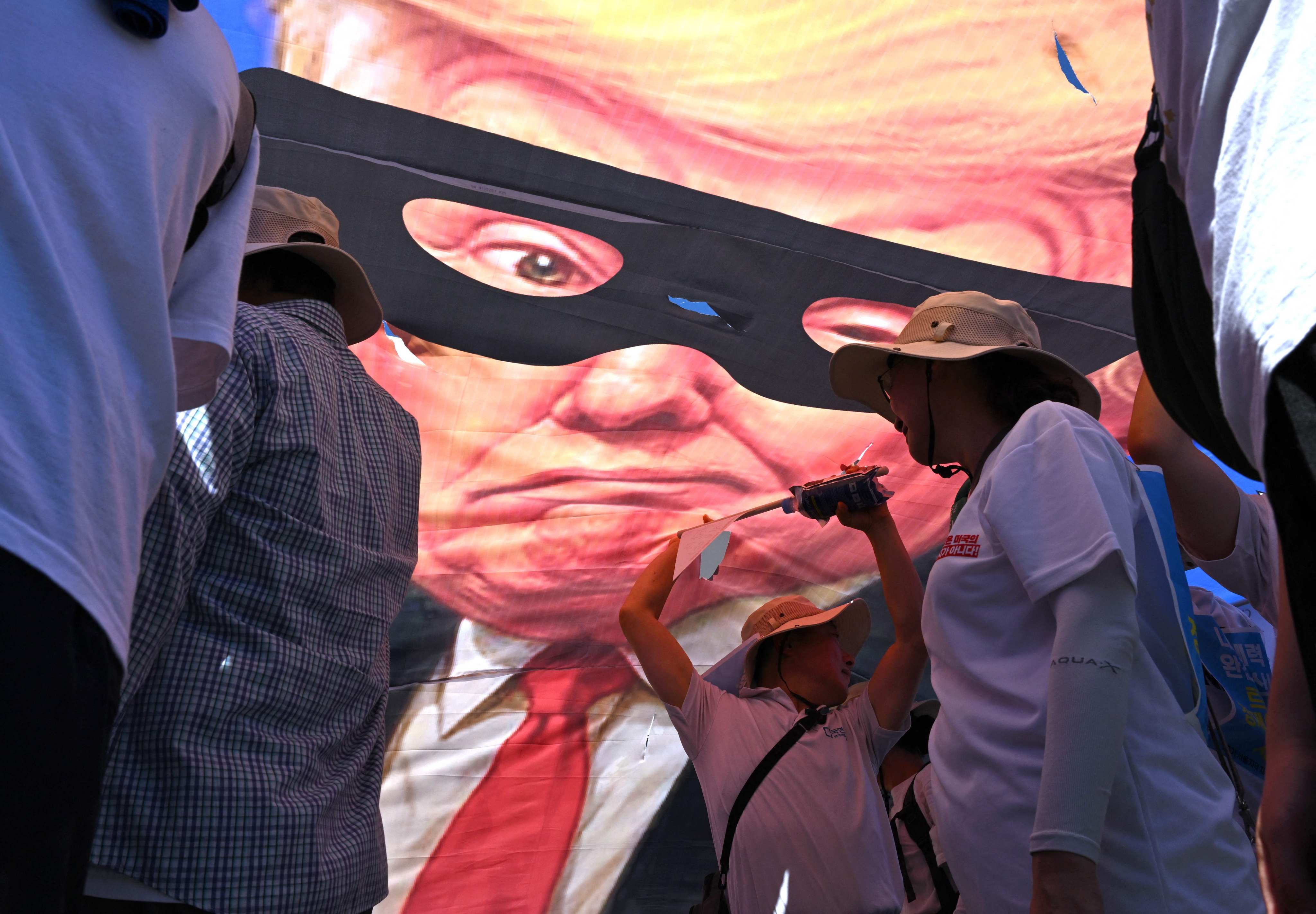 South Korean protesters tear a banner showing a caricature of US President Donald Trump as a robber during a rally in Seoul against Washington’s tariff policy on July 27. Photo: AFP