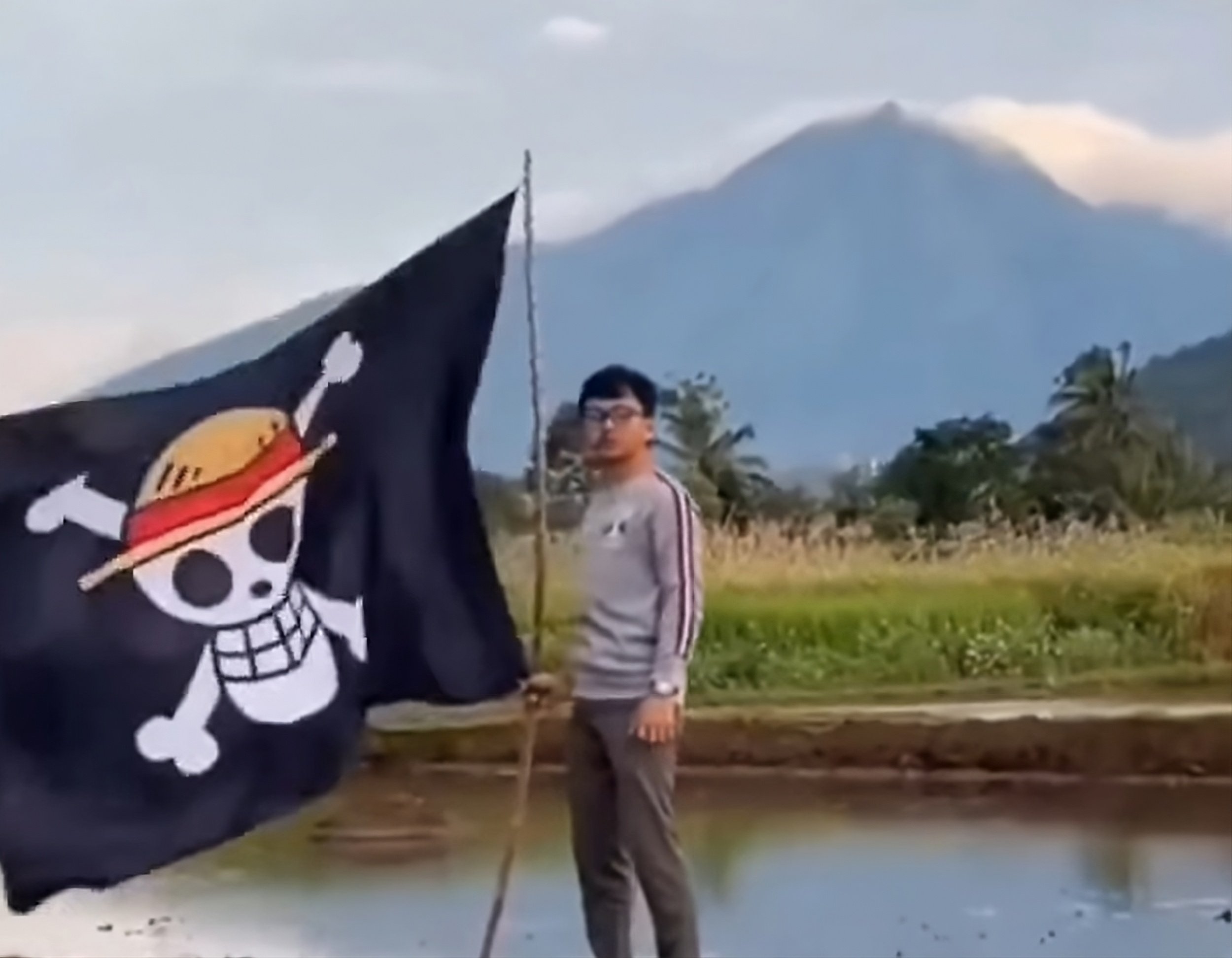 A man in Indonesia holds a One Piece flag with an active volcano in the background. Photo: Facebook