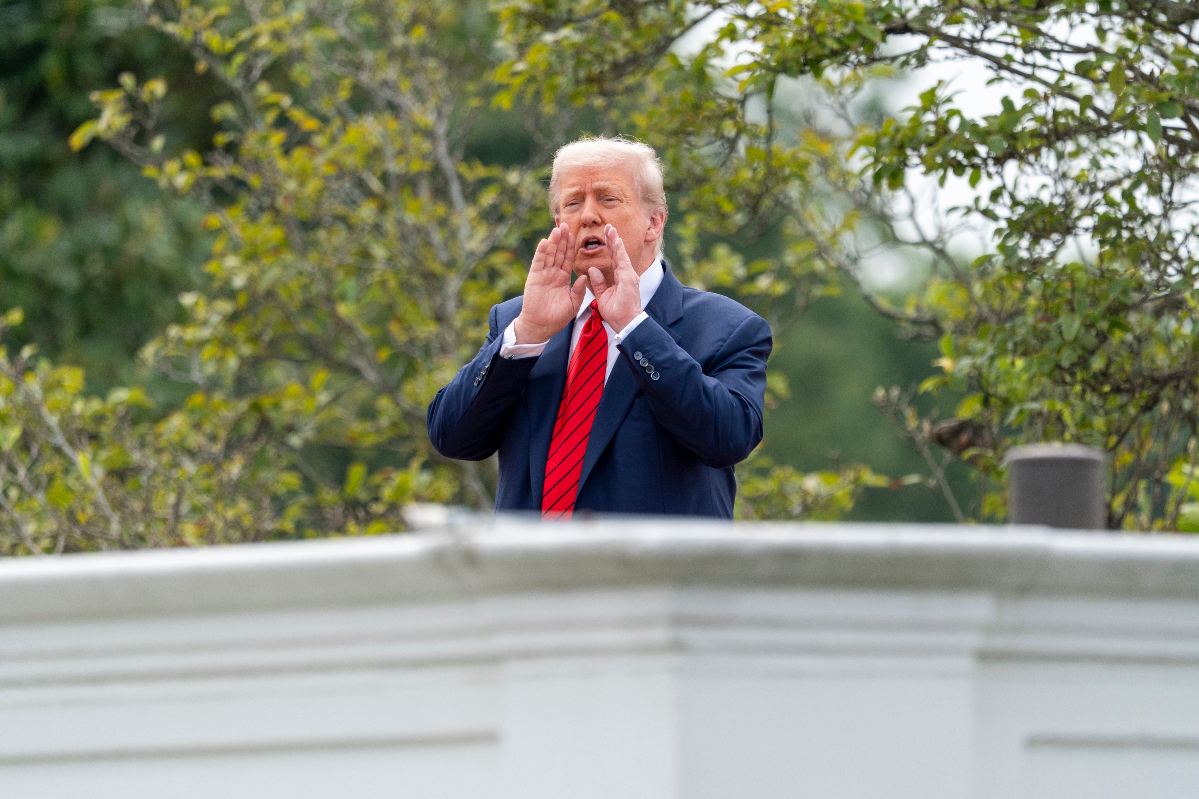 President Donald Trump shouts to reporters as he surveys the grounds from the roof above the Colonnade that goes to the West Wing of the White House, Tuesday, Aug. 5, 2025, in Washington. (AP Photo/Alex Brandon)