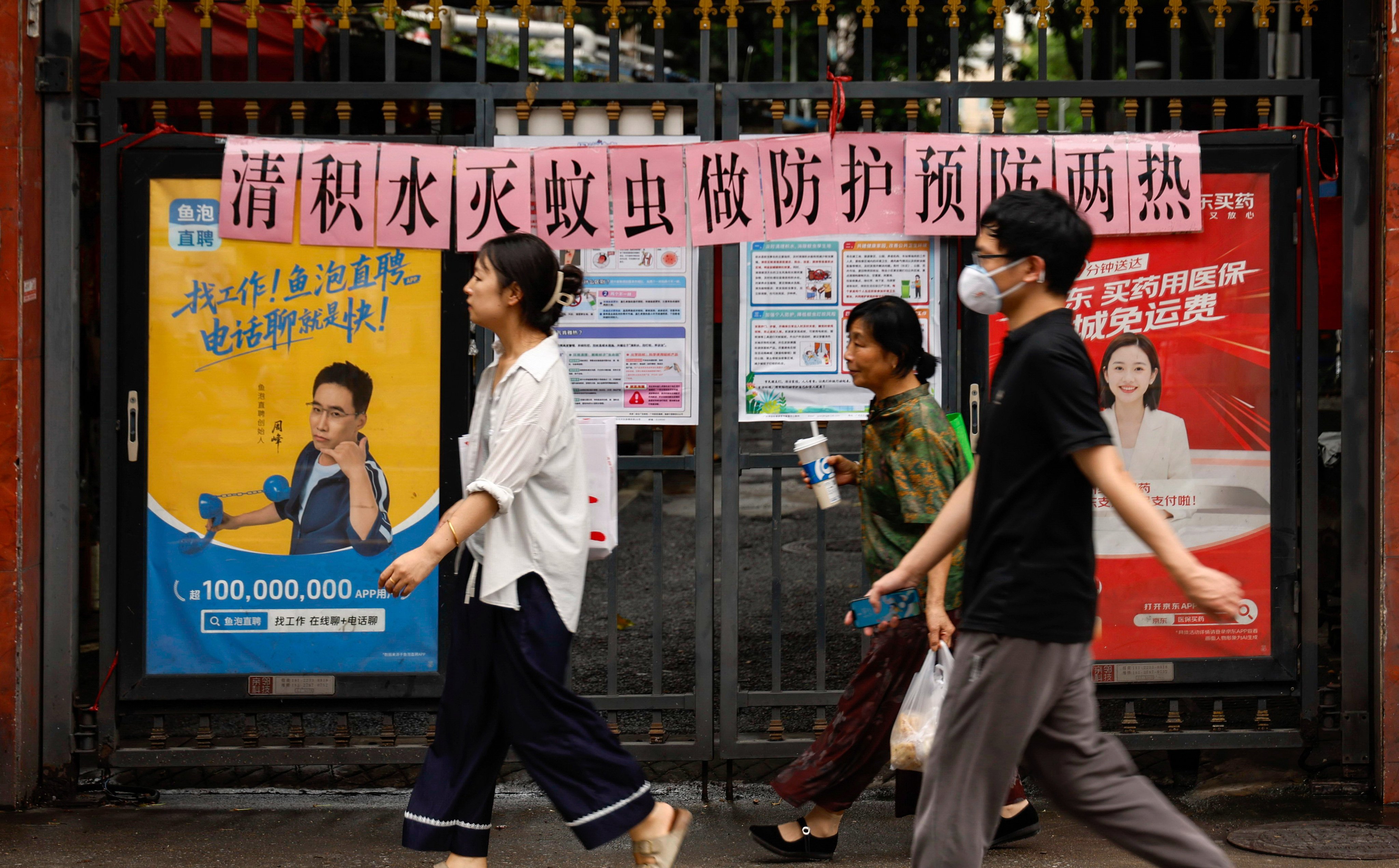 Residents walk past a residential entrance gate displaying a slogan urging mosquito control, in Guangzhou, south China’s Guangdong province. Photo: Chinatopix via AP