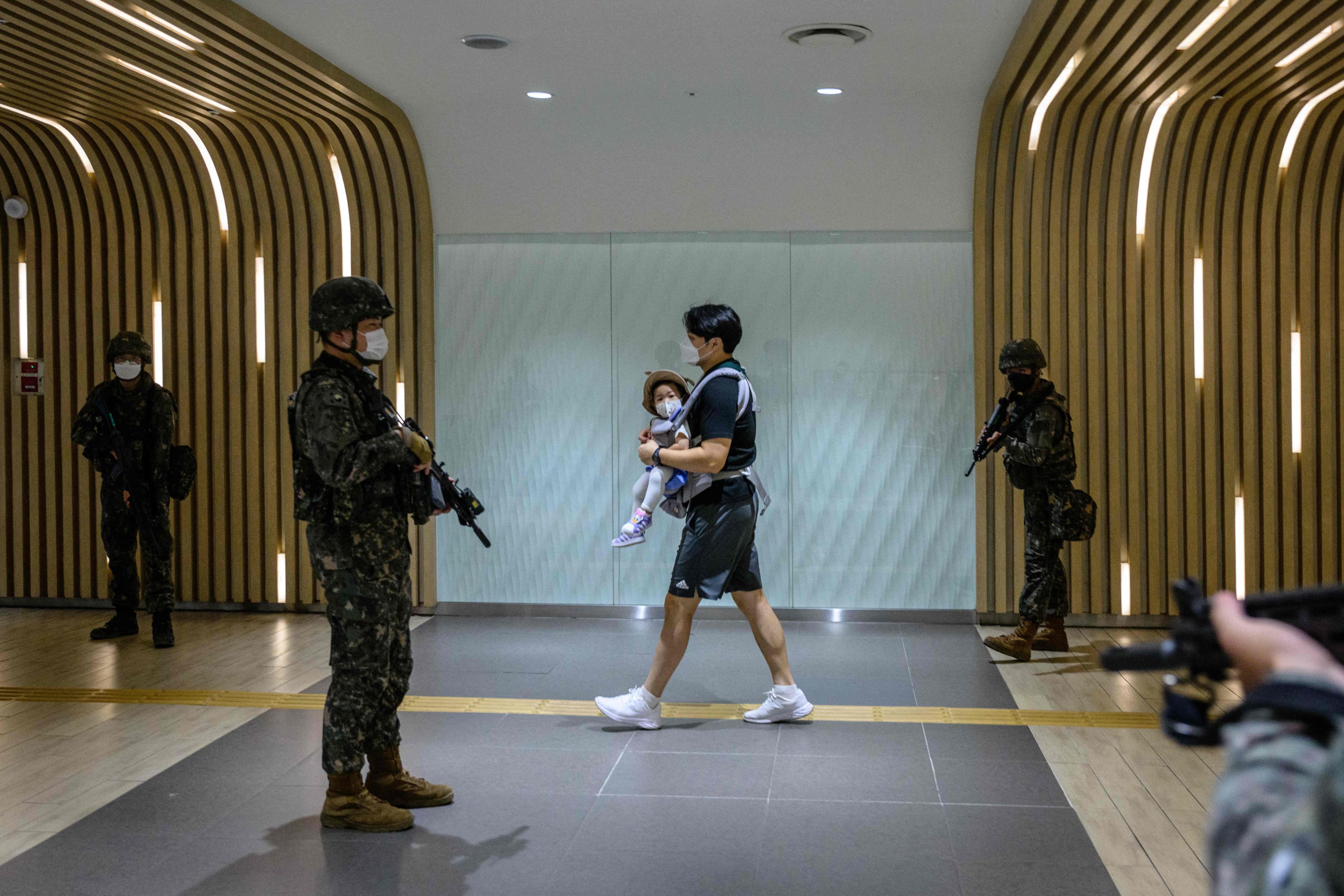 A man carries a baby as he walks past South Korean soldiers during an anti-terror drill at a shopping centre in Seoul in 2022. Photo: AFP