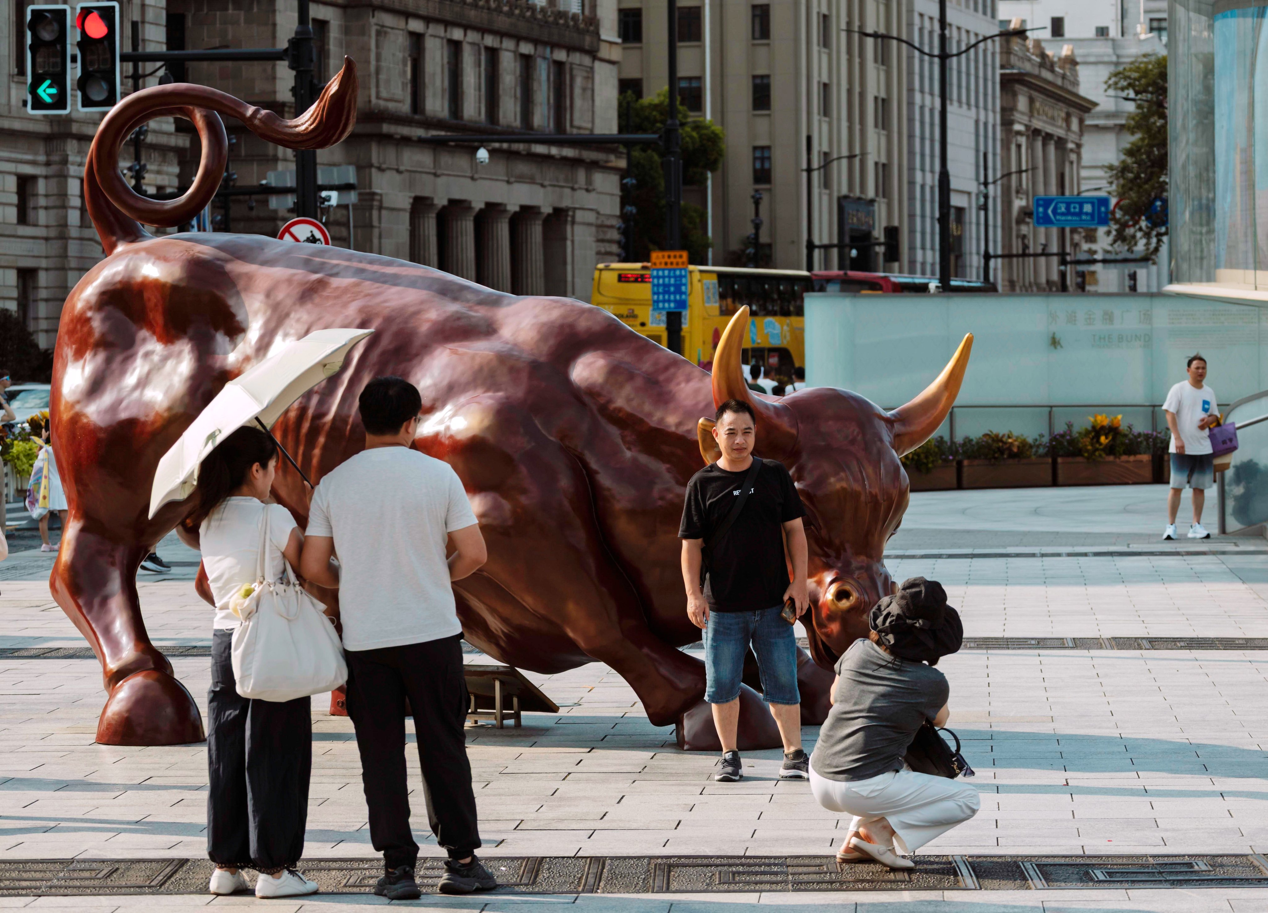 People pose near a bull statue in Shanghai on August 7, 2025. Photo: EPA