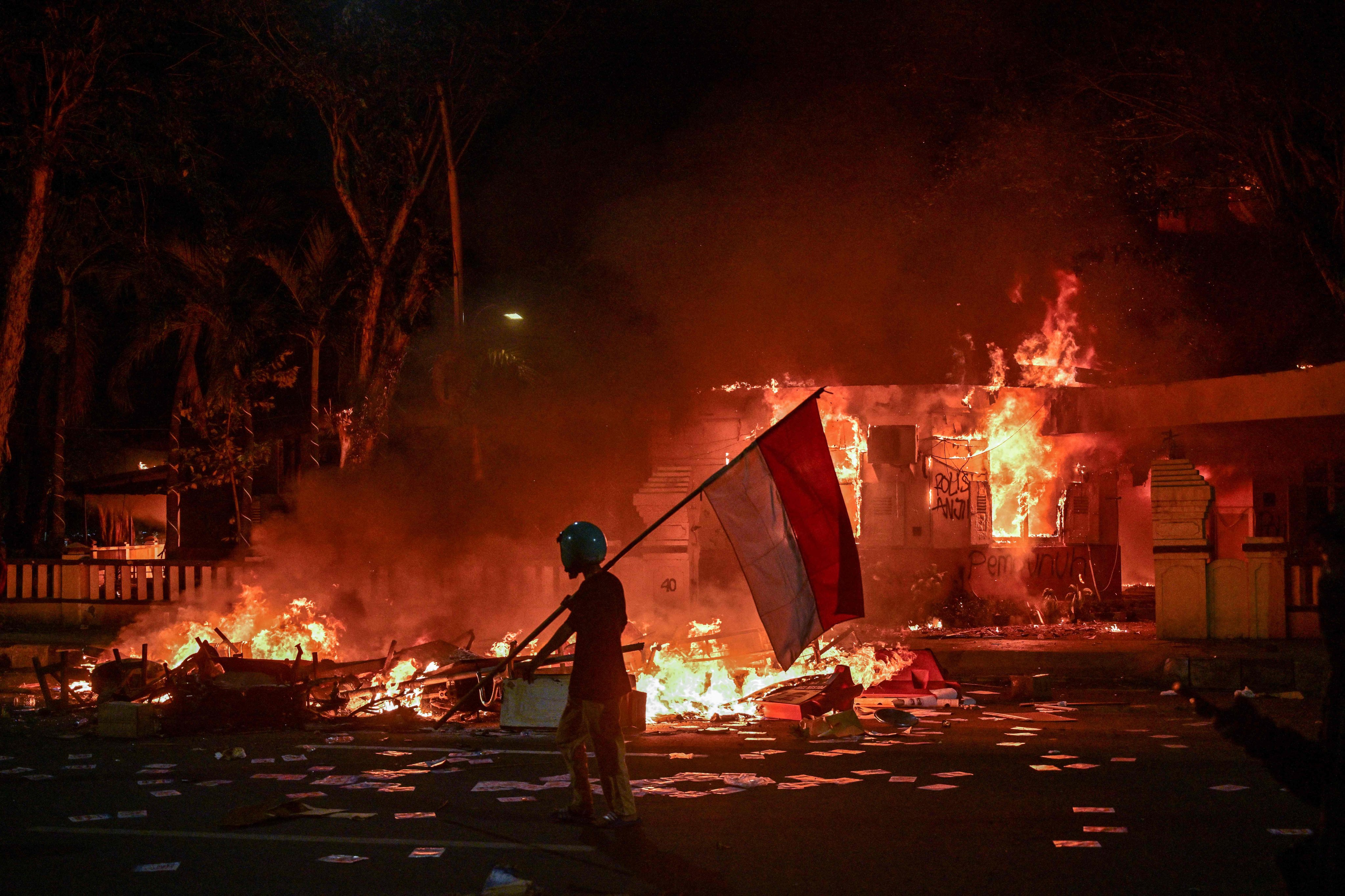 A protester walks with an Indonesian flag in front of a police headquarters that was set on fire in Surabaya on August 31. Photo: AFP