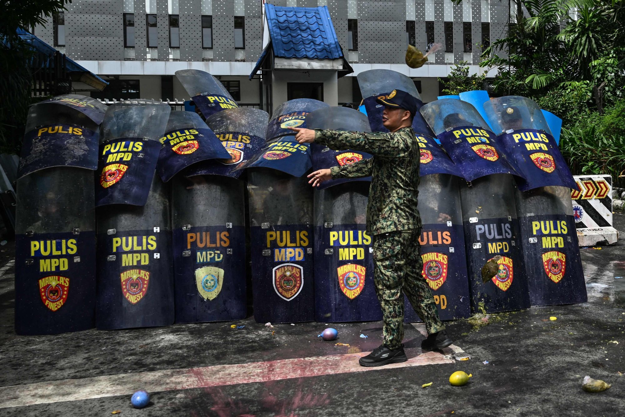 Policemen use their shields for protection as protesters throw balloons filled with dirty water outside the Department of Public Works and Highways on Thursday. Photo: AFP