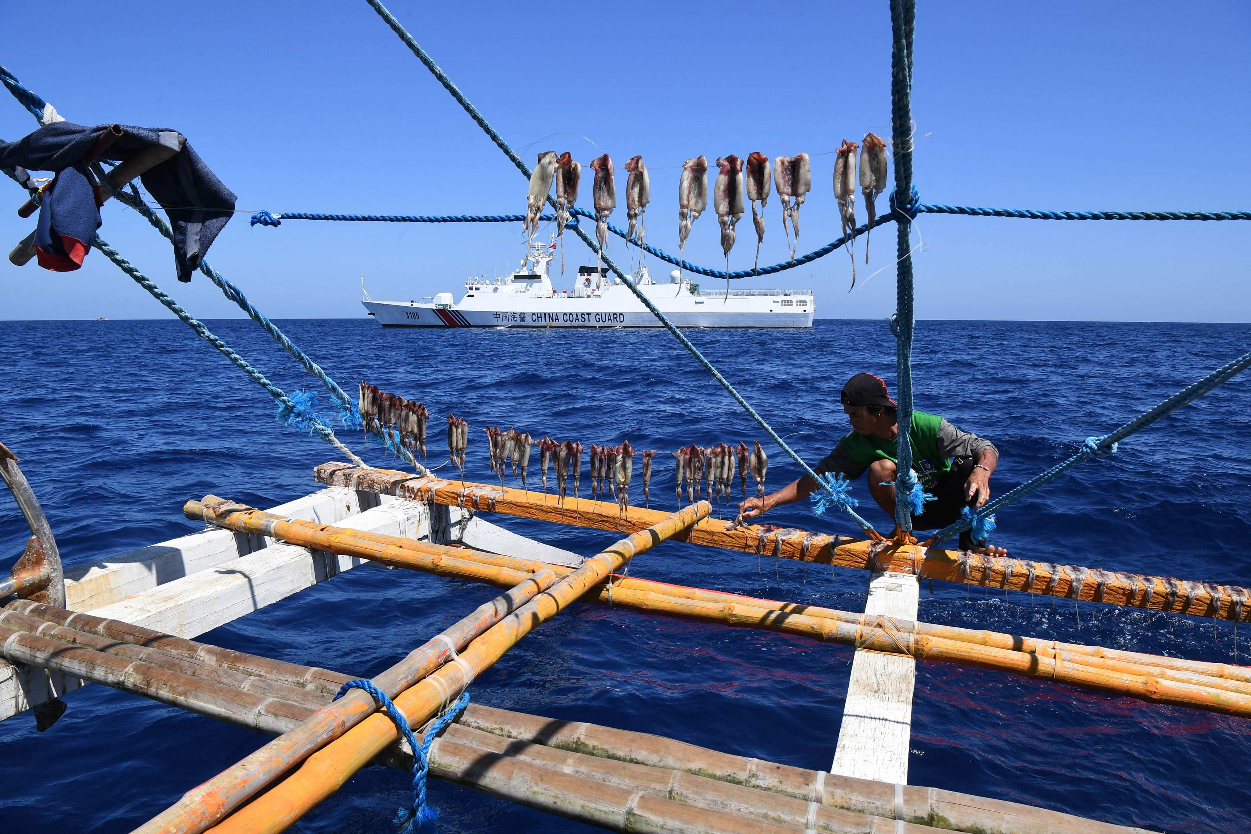 A Filipino fisherman dries squid on a fishing boat in the South China Sea with a Chinese coastguard ship in the background. Photo: AFP