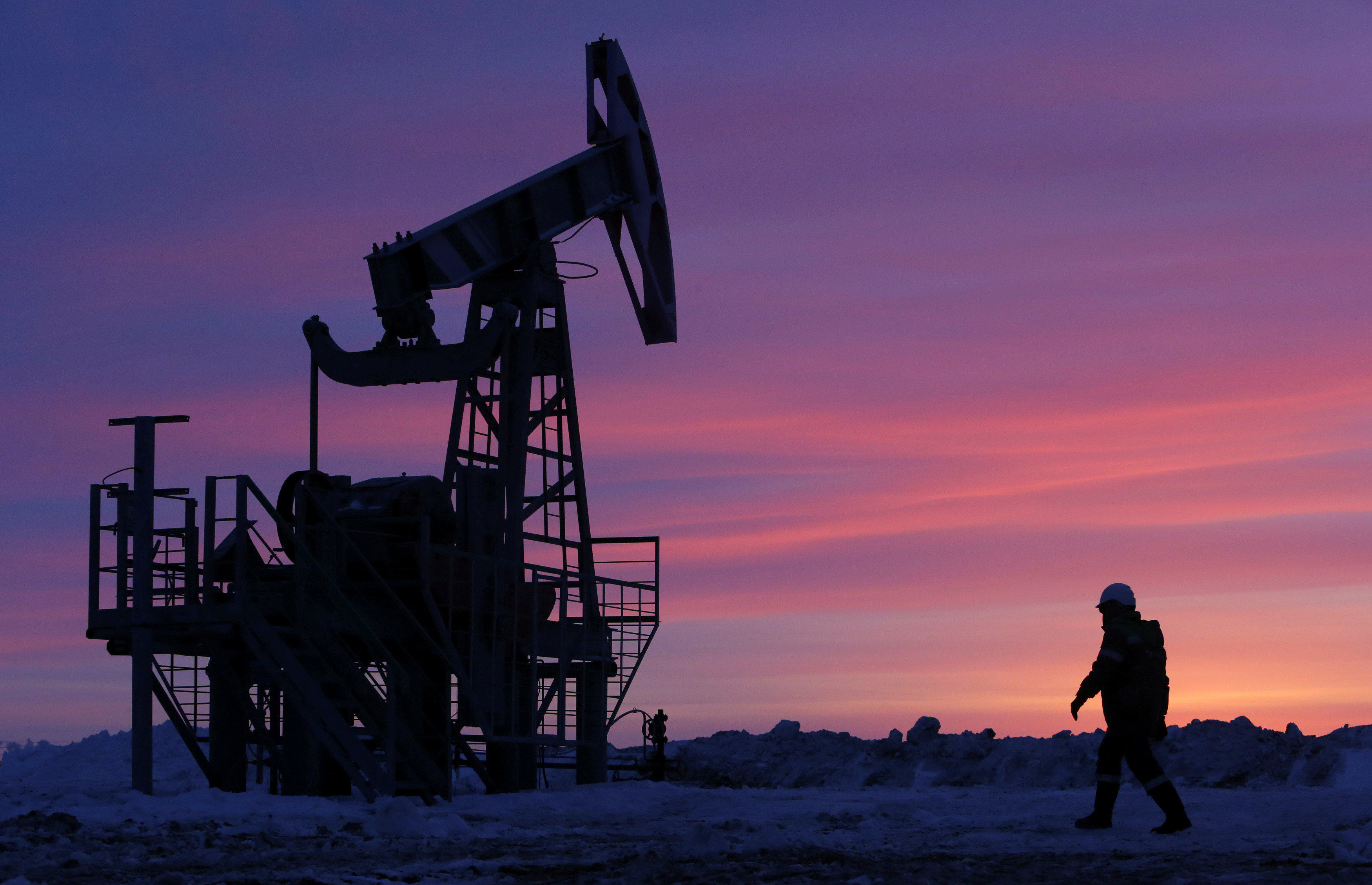 A worker walks past a pump jack on an oil field owned by the Bashneft company near Nikolo-Berezovka, Bashkortostan, Russia, in January 2015. Photo: Reuters