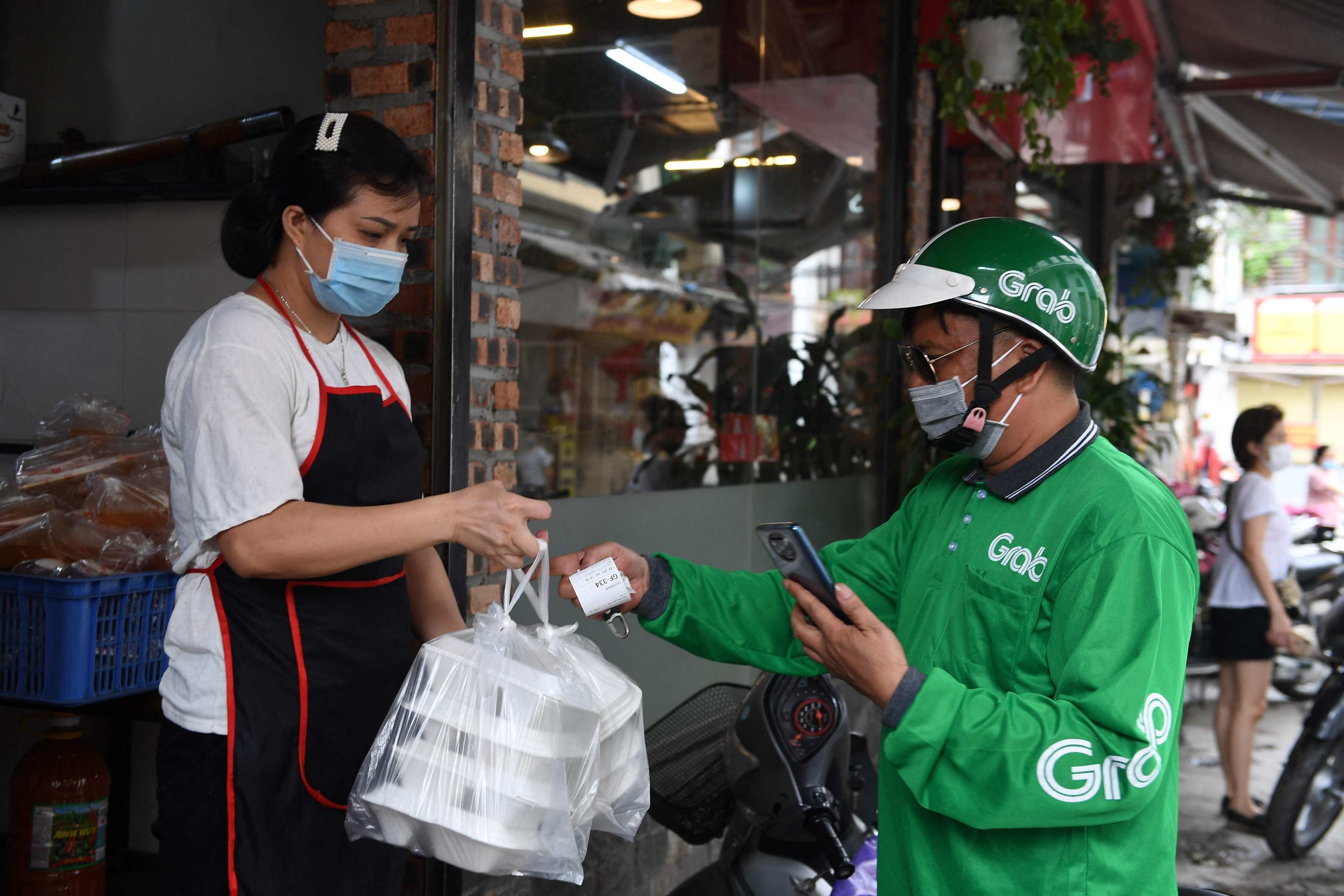A Grab delivery service worker receives a takeaway food order from a restaurant in Hanoi, Vietnam on May 25, 2021. Photo: AFP