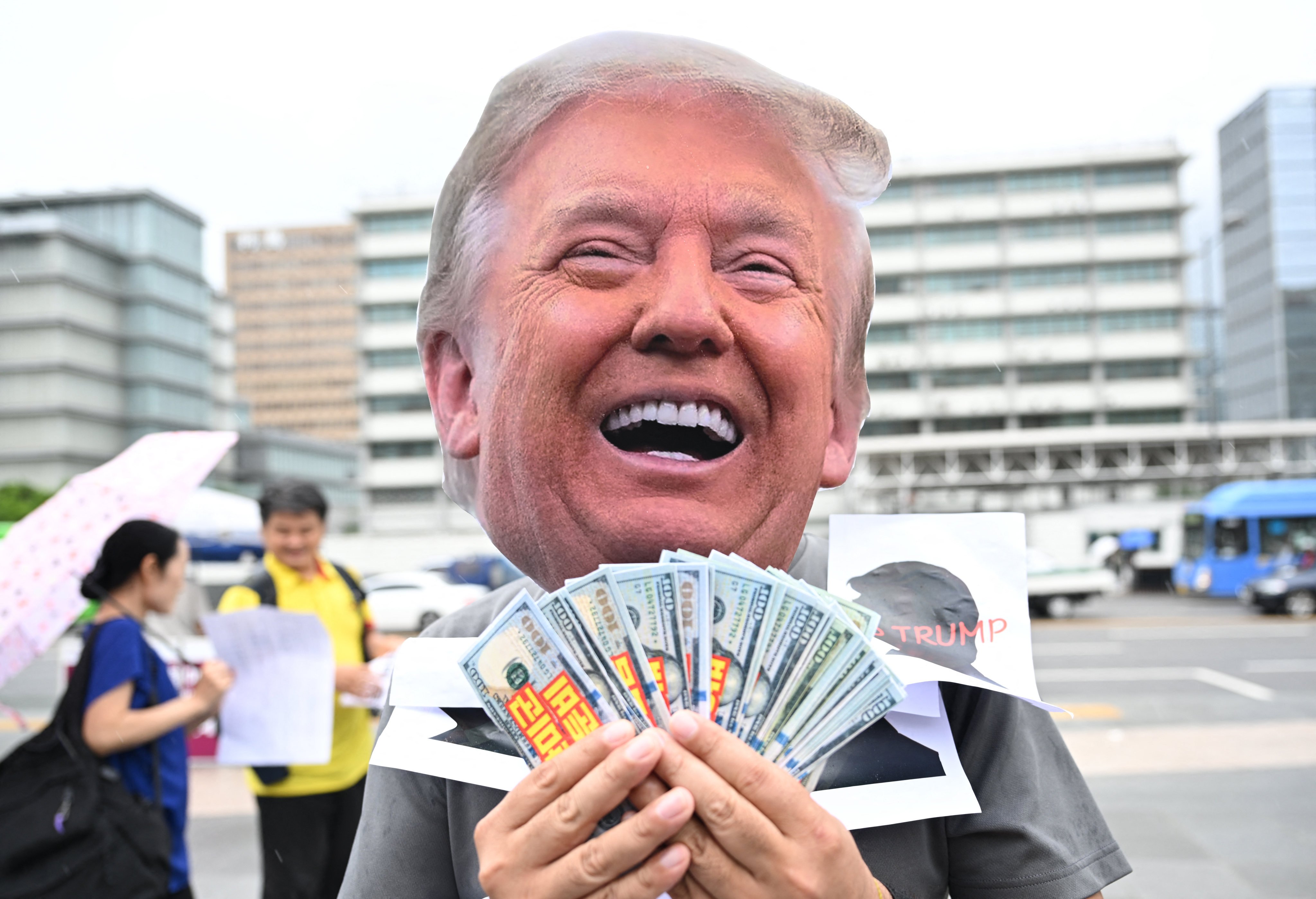 A protester holding US dollar banknotes wears a mask of Donald Trump during a rally in July against Trump’s tariff policy near the US embassy in Seoul. Photo: AFP