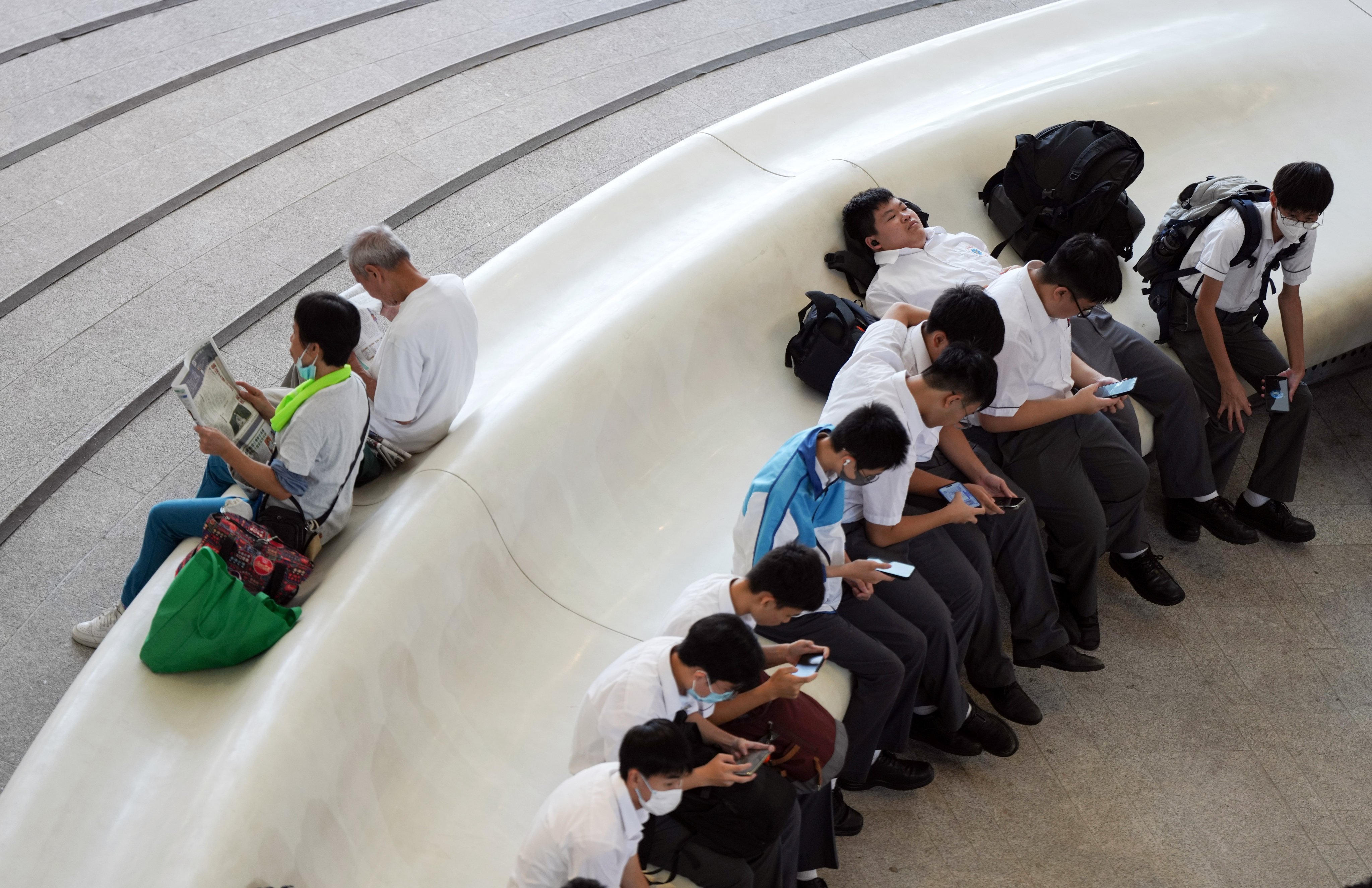 Students look at their phones as seniors read newspapers, at the Xiqu Centre in Tsim Sha Tsui on October 14, 2024. Photo: Eugene Lee