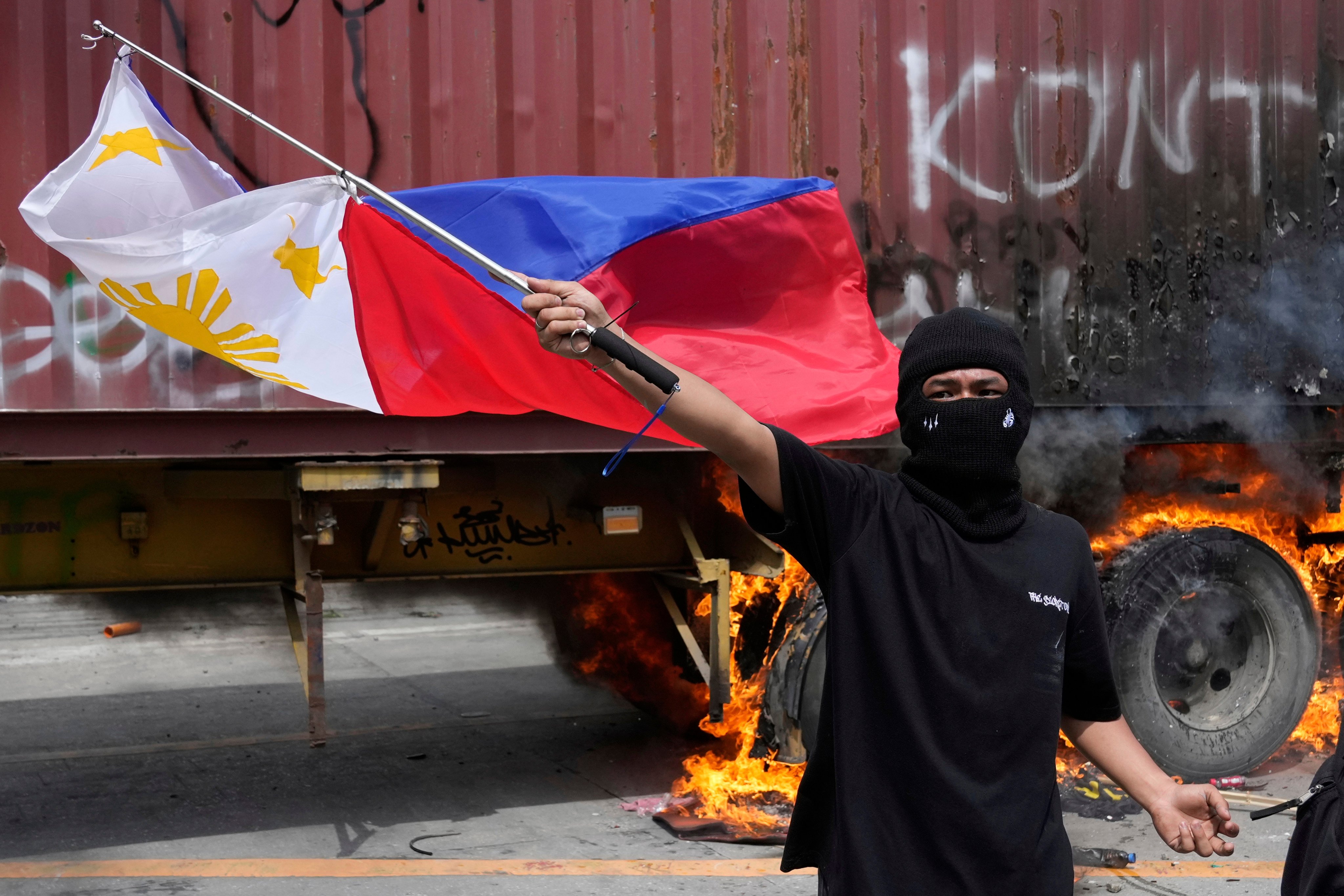 A protester waves a Philippine flag beside a burning container truck as they clash with police while trying to enter the Malacanang presidential palace compound in Manila on Sunday. Photo: AP