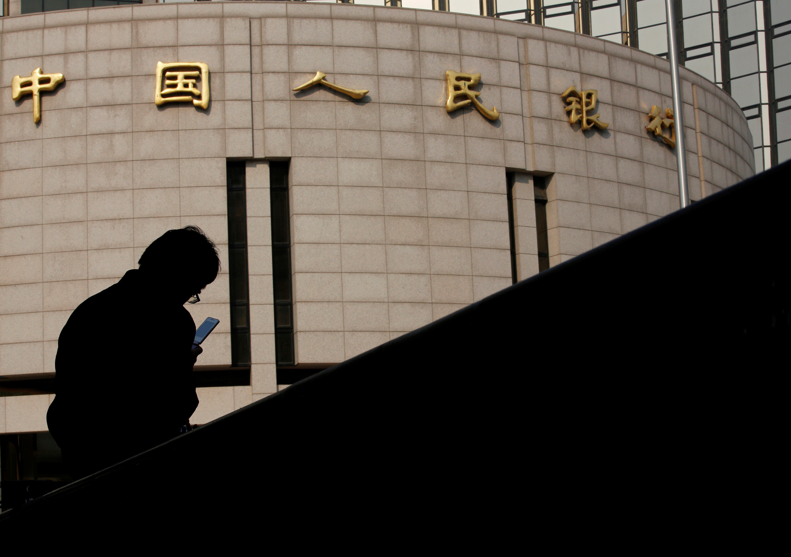 A man sits in front of the headquarters of the People’s Bank of China, the country’s central bank, in Beijing. Photo: Reuters