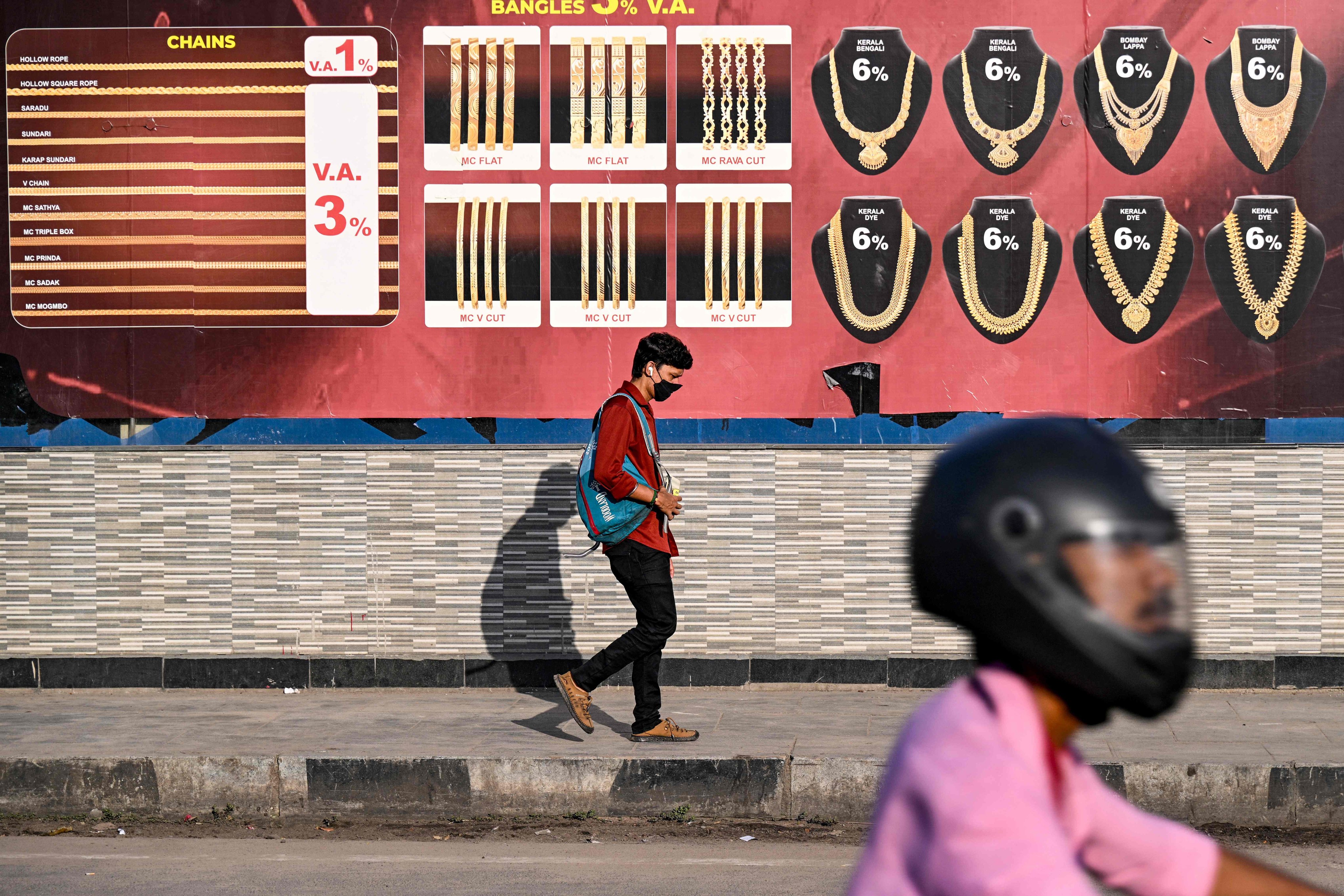 A man walks past an advertisement of gold jewellery displayed on a wall in Chennai on August 25. The disruptions caused by the US tariffs go beyond reduced output, spreading into people losing their jobs, workplaces closing and a compounding effect across supply chains and service providers. Photo: AFP