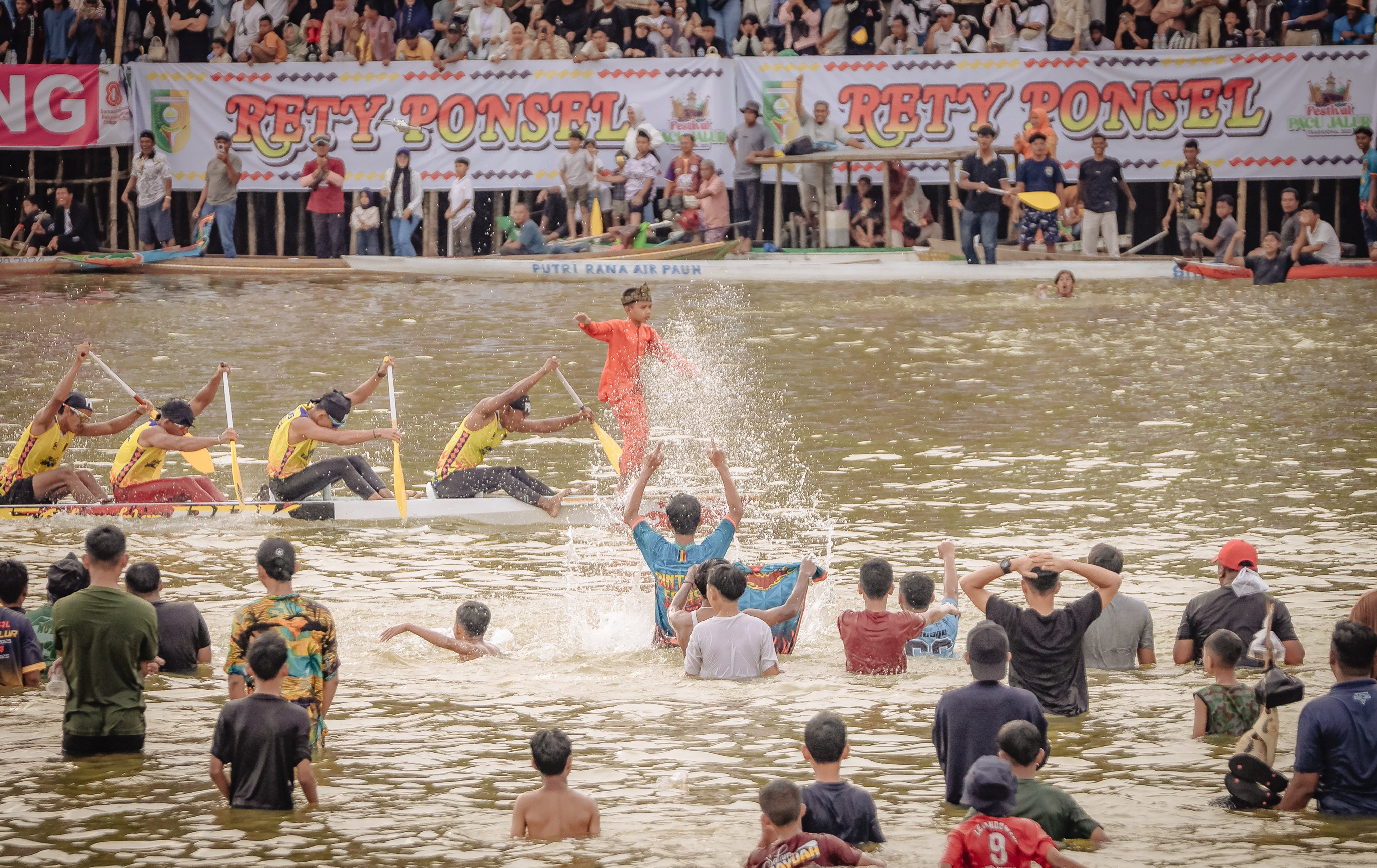 A young boy stands at the bow of a boat as spectators in the river cheer passionately for their favorite team during the 2025 Pacu Jalur Festival on August 24, in Kuantan Singingi Regency, Riau Province, Indonesia. Photo: Afrianto Silalahi
