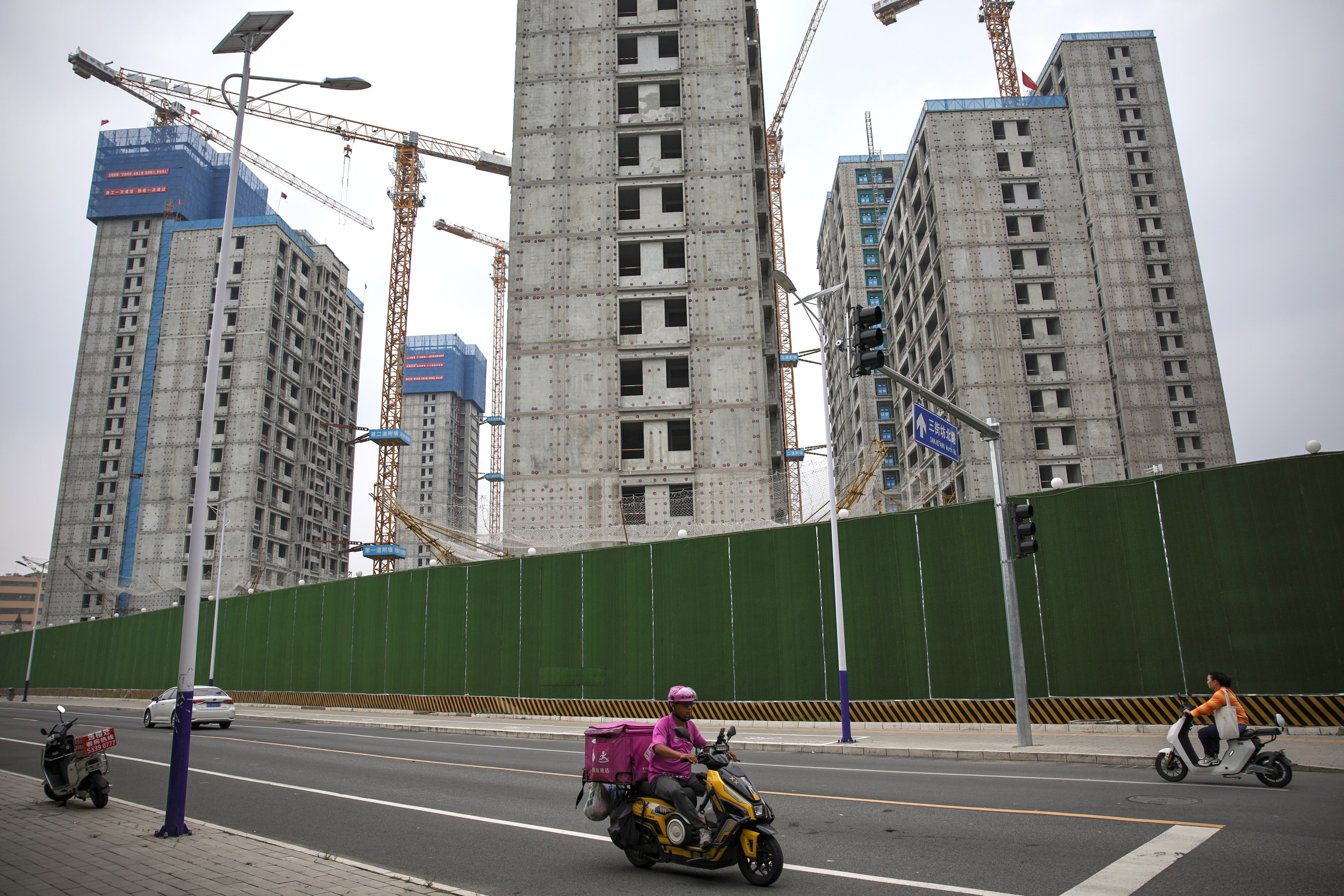 People ride electric scooters past buildings under construction in Beijing last month. Photo: EPA