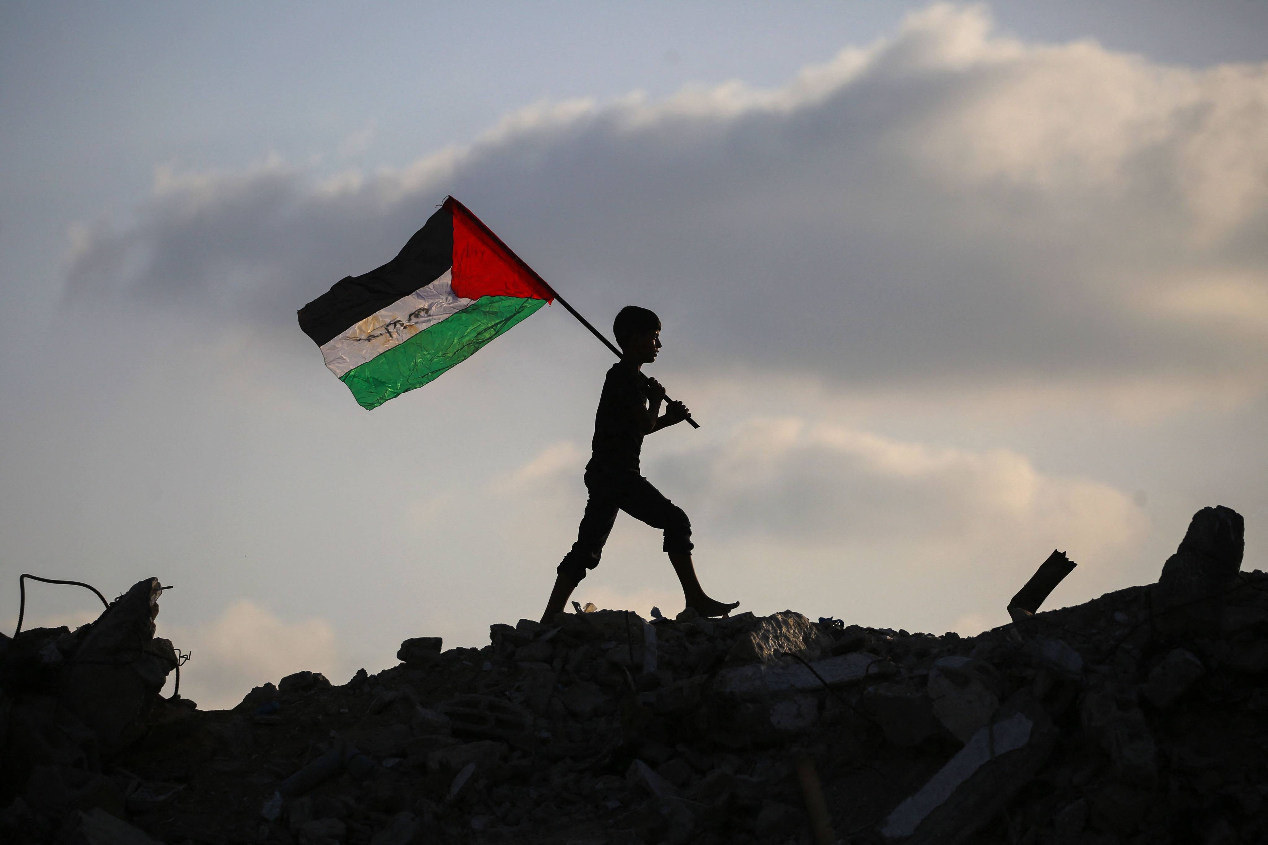 A displaced Palestinian child waves a Palestinian national flag as he walks on the rubble of a destroyed building in the central Gaza Strip on September 22. Photo: AFP