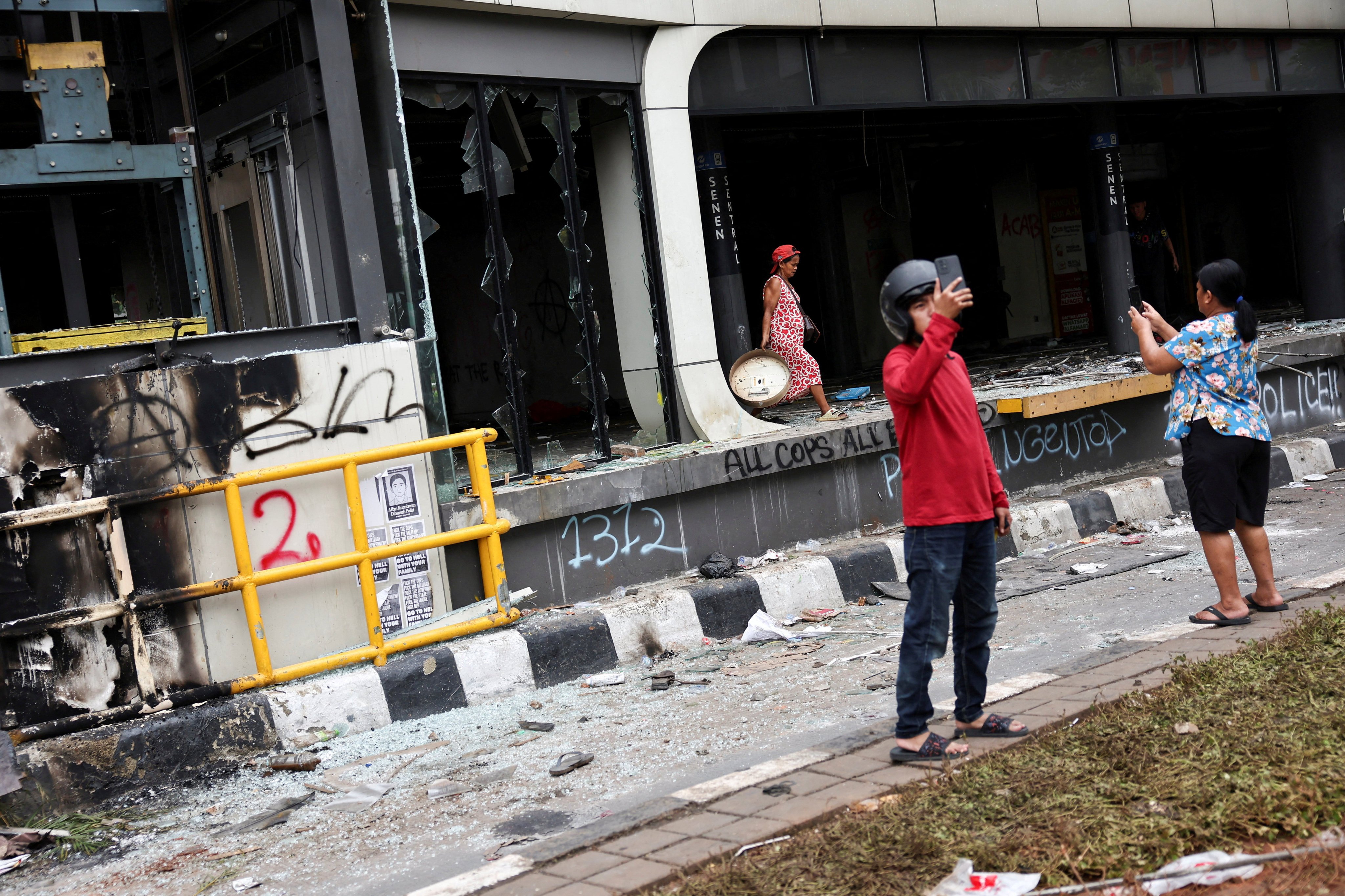 People use their phones to take photos of a bus stop burned during a protest over lawmakers’ pay on August 30. Photo: Reuters