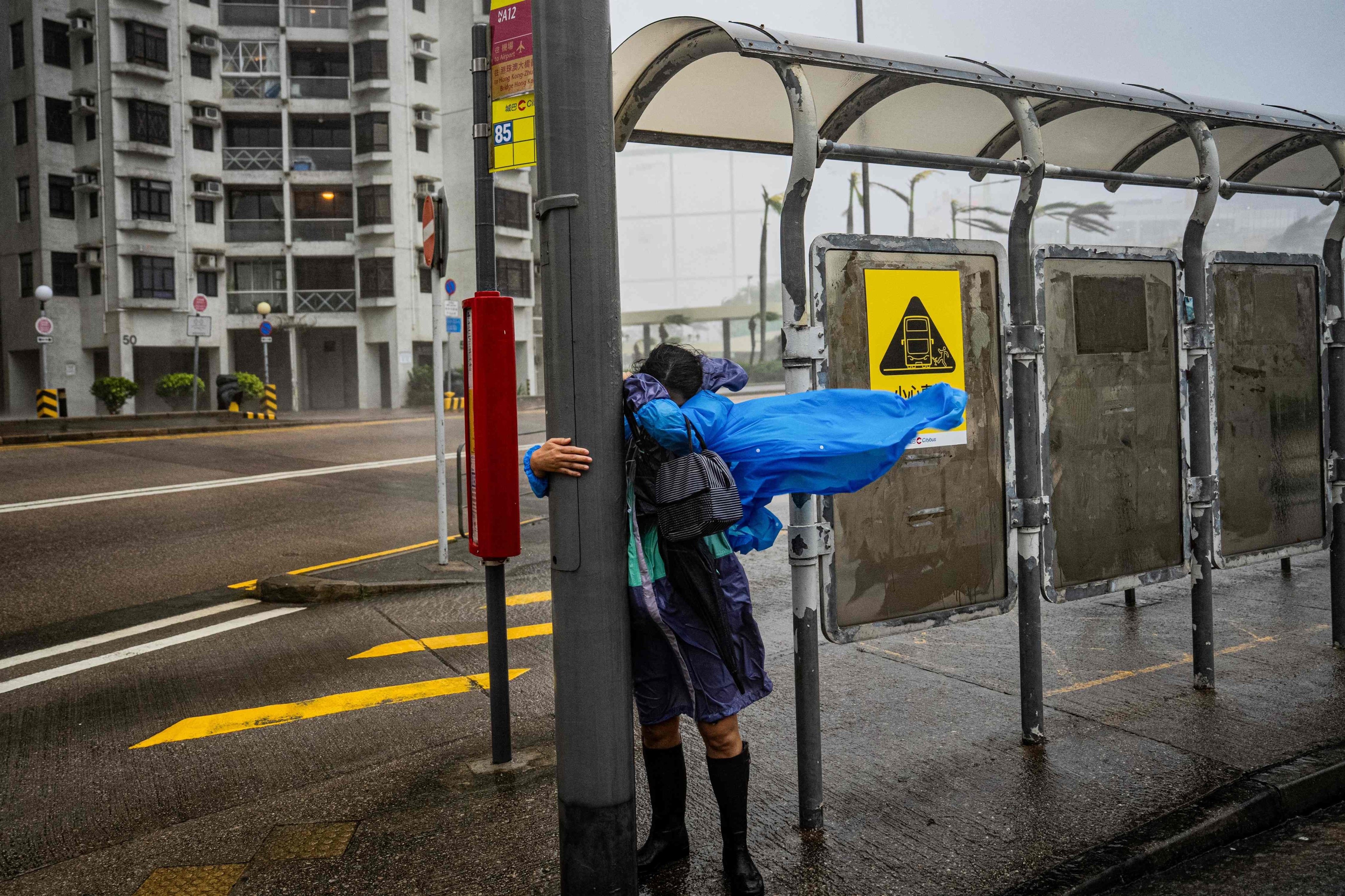 A woman holds onto a lamppost at a bus stop in Heng Fa Cheun as Super Typhoon Ragasa hits Hong Kong on September 24. Climate change is profoundly impacting society, including mental health. Photo: AFP