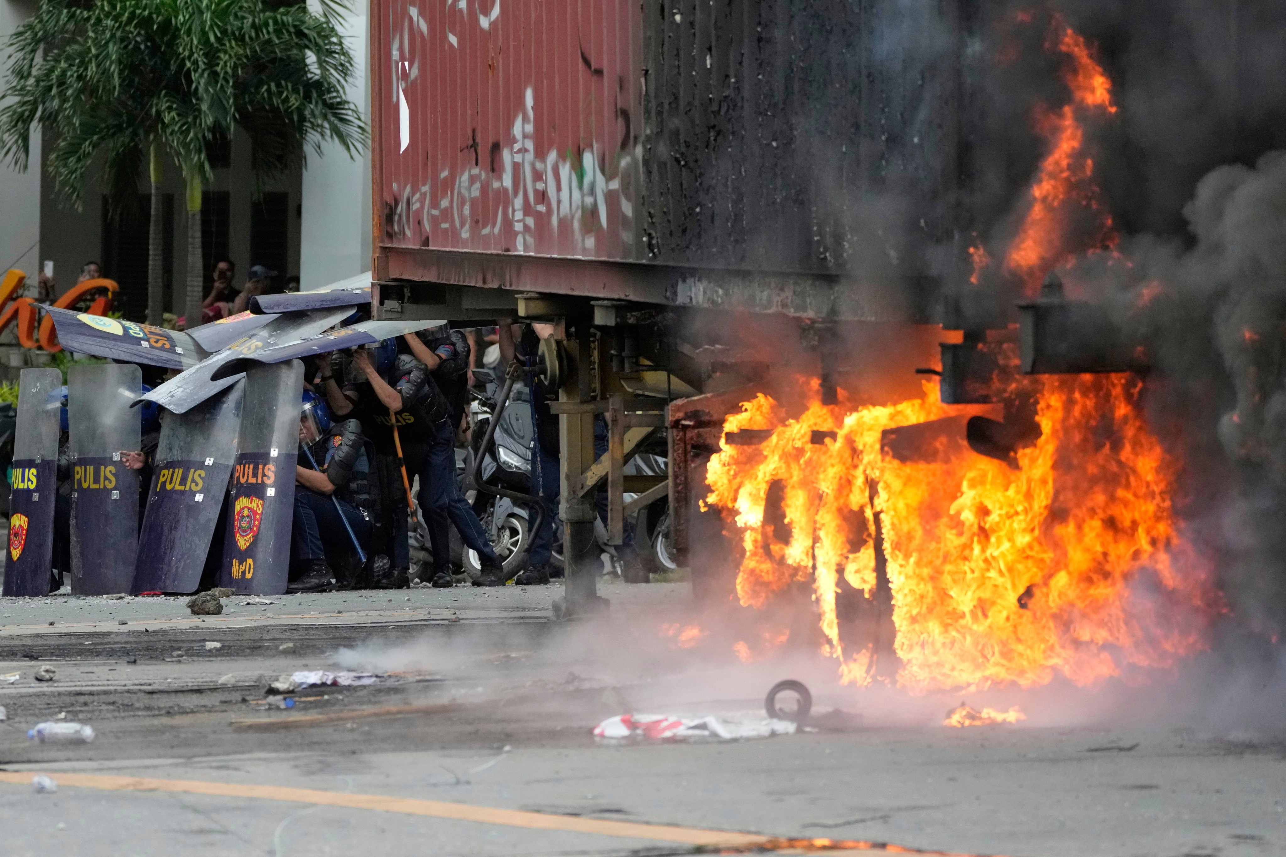 Police shield themselves beside a burning container during clashes with anti-corruption protesters in Manila on September 21. Photo: AP