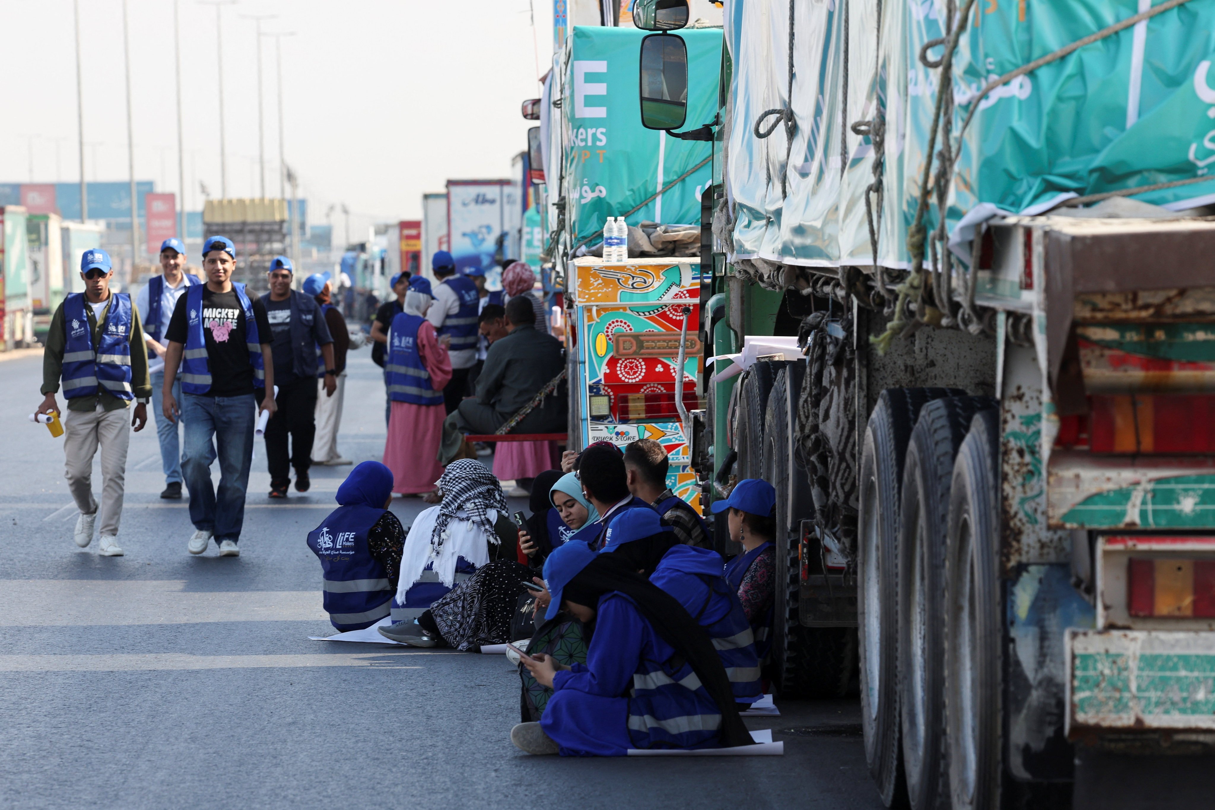 Egyptian volunteers rest and sit next to trucks loaded with humanitarian aid as they wait to enter Gaza through the Rafah crossing. Photo: Reuters