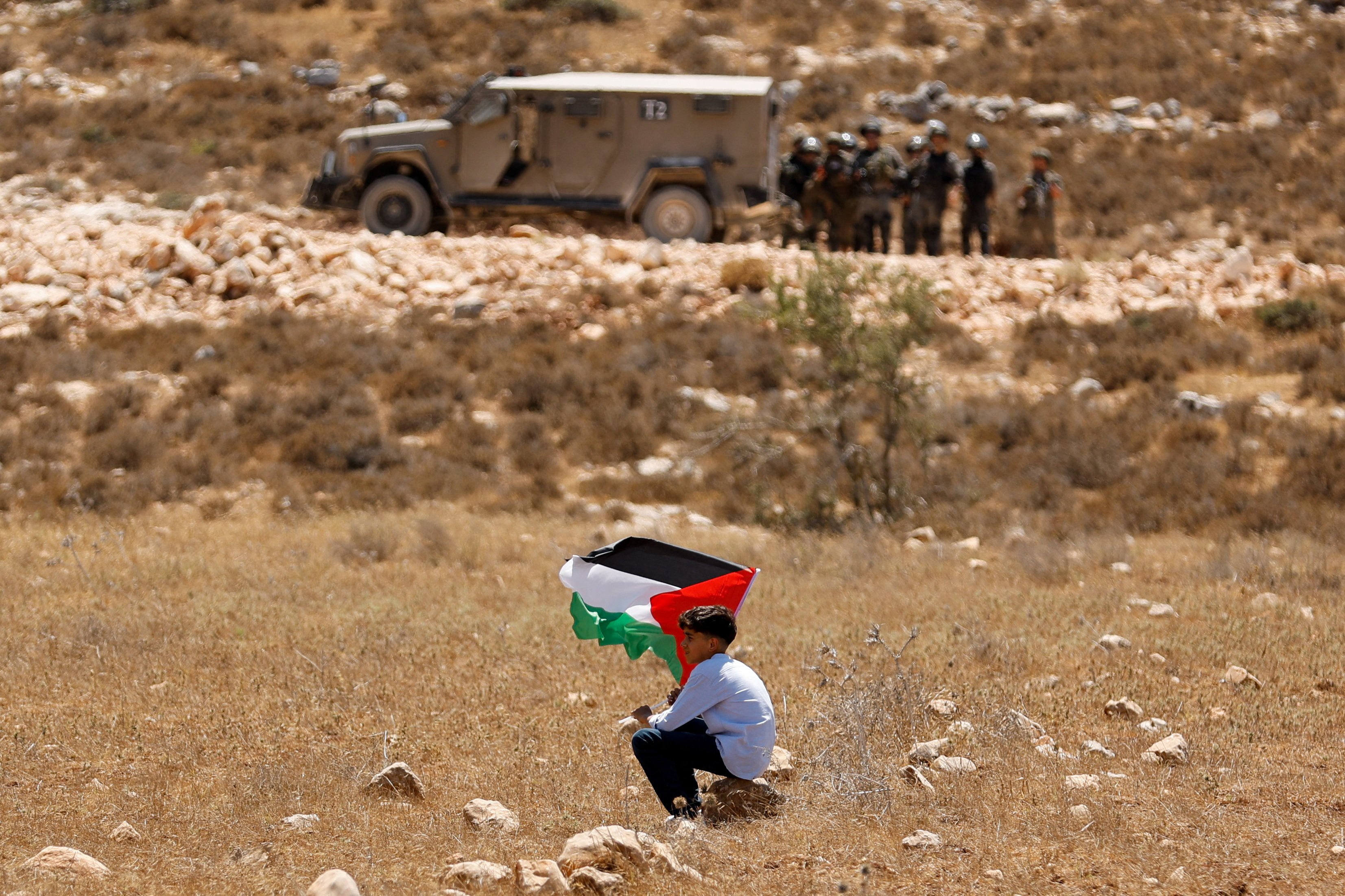 A boy holds a Palestinian flag during a demonstration against what Palestinians say is Israel’s confiscation of their land, as Israeli security forces stand guard, in the Israeli-occupied West Bank. Photo: Reuters