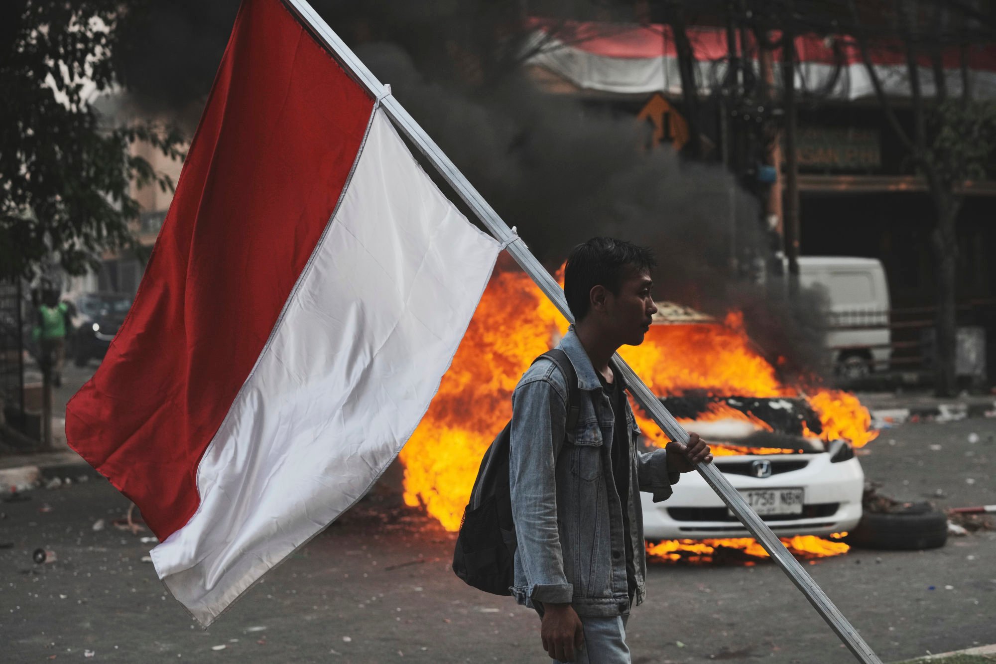 A man carries an Indonesian national flag near a burning car in clashes between riot police and students protesting against lawmakers’ allowances, in Jakarta, Indonesia, on August 29. Photo: AP A man carries an Indonesian national flag near a burning car in clashes between riot police and students protesting against lawmakers’ allowances, in Jakarta, Indonesia, on August 29. Photo: AP