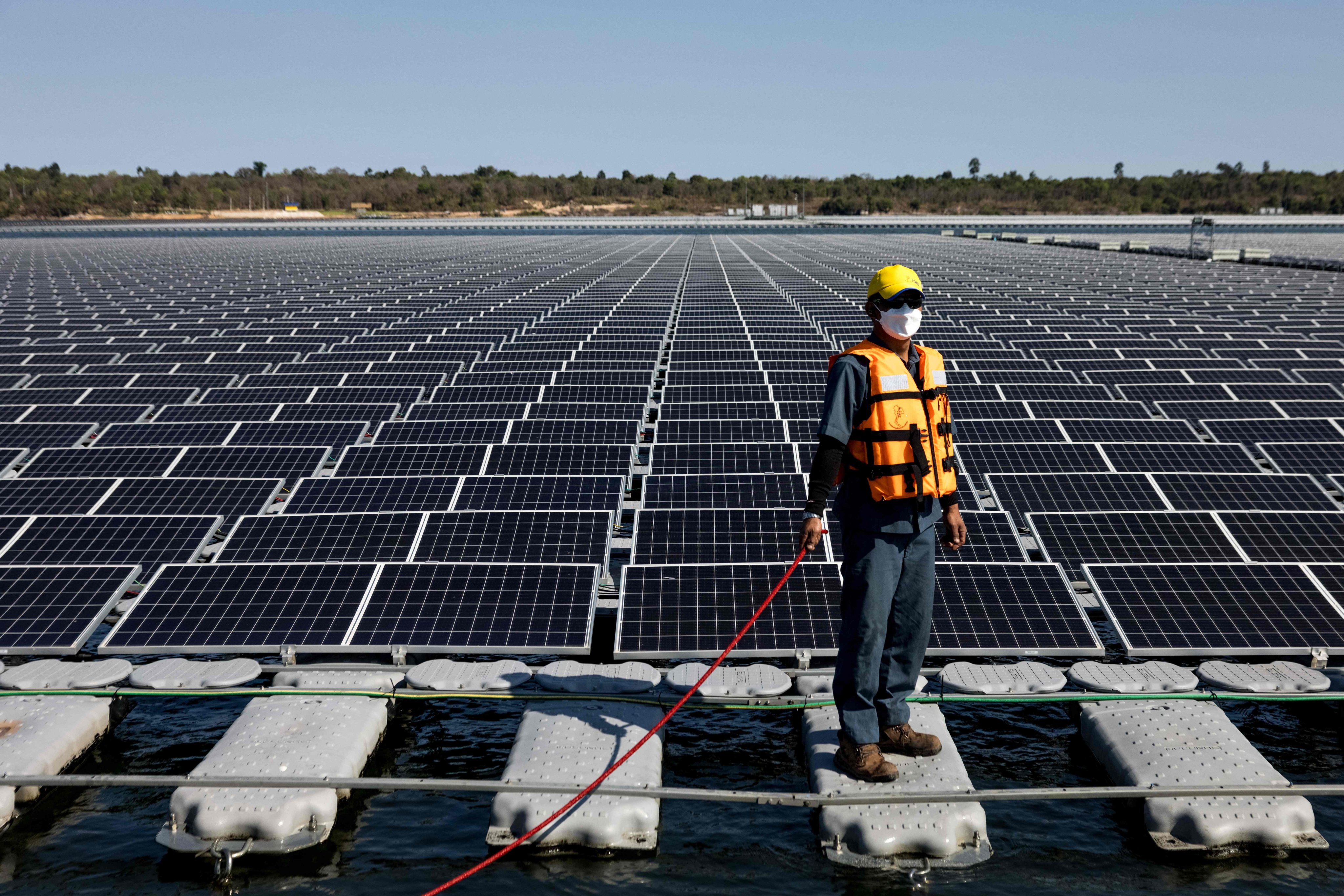 A worker stands beside floating solar panels for a hydro-solar farm in Thailand. Photo: AFP