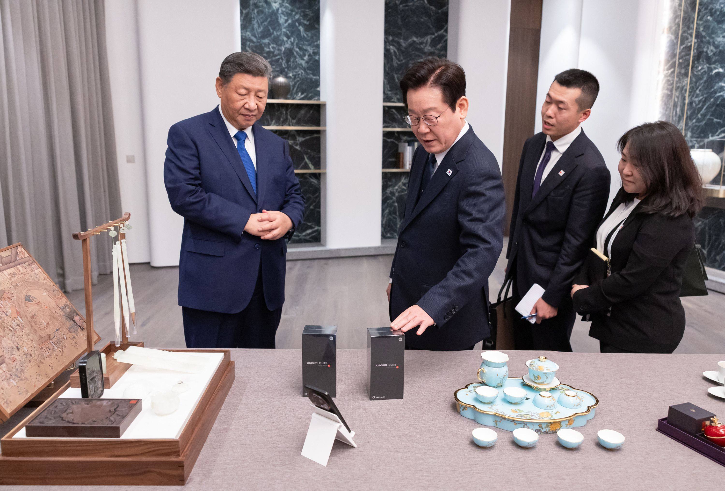 South Korea’s President, Lee Jae-myung, taps the box of one of the Xiaomi smartphones presented as gifts by Chinese President Xi Jinping, left, during their meeting on November 1, as their respective interpreters look on. Photo: AFP