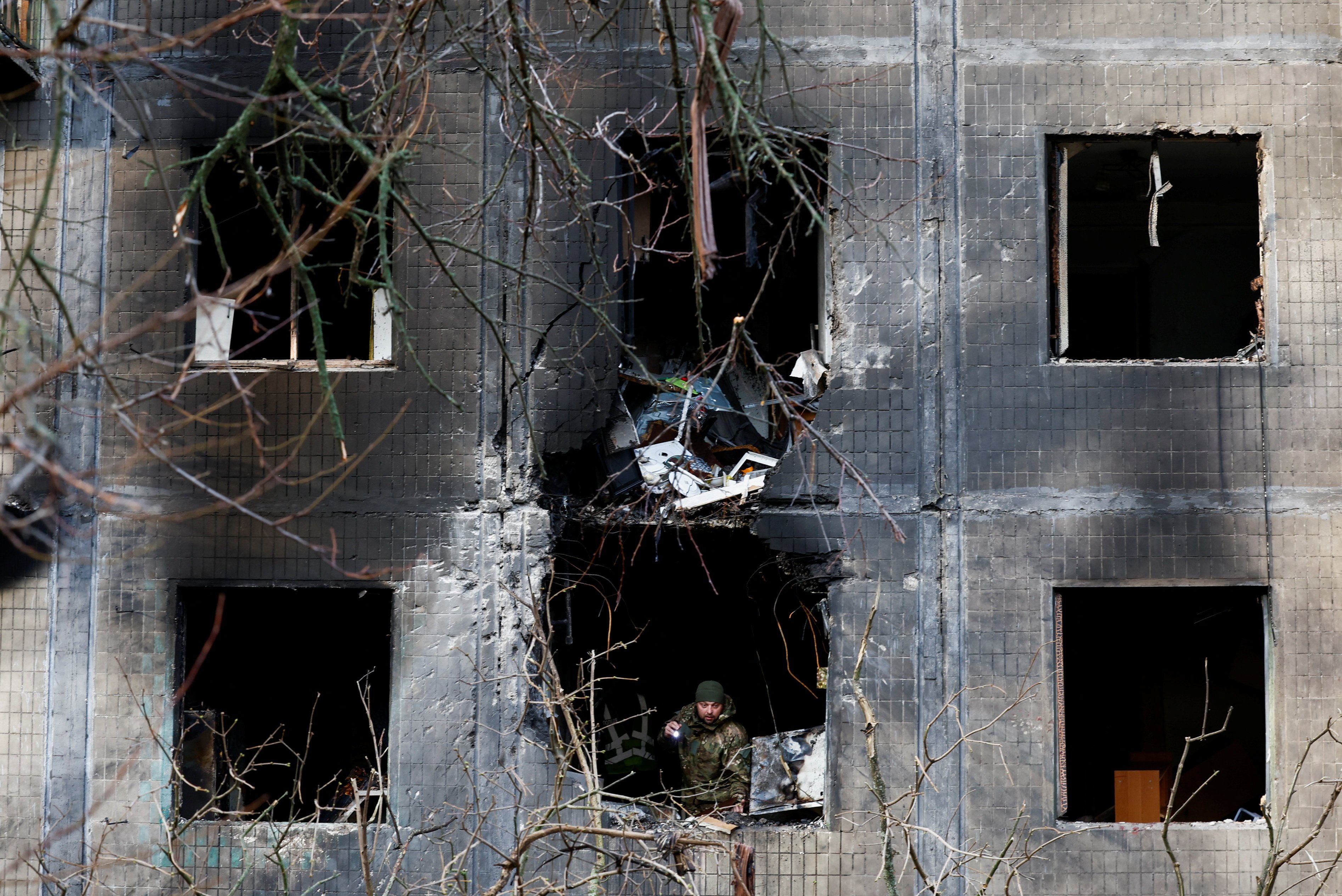 An investigator looks through the window of a Kyiv residential building after an overnight Russian drone and missile strike. Photo: Reuters