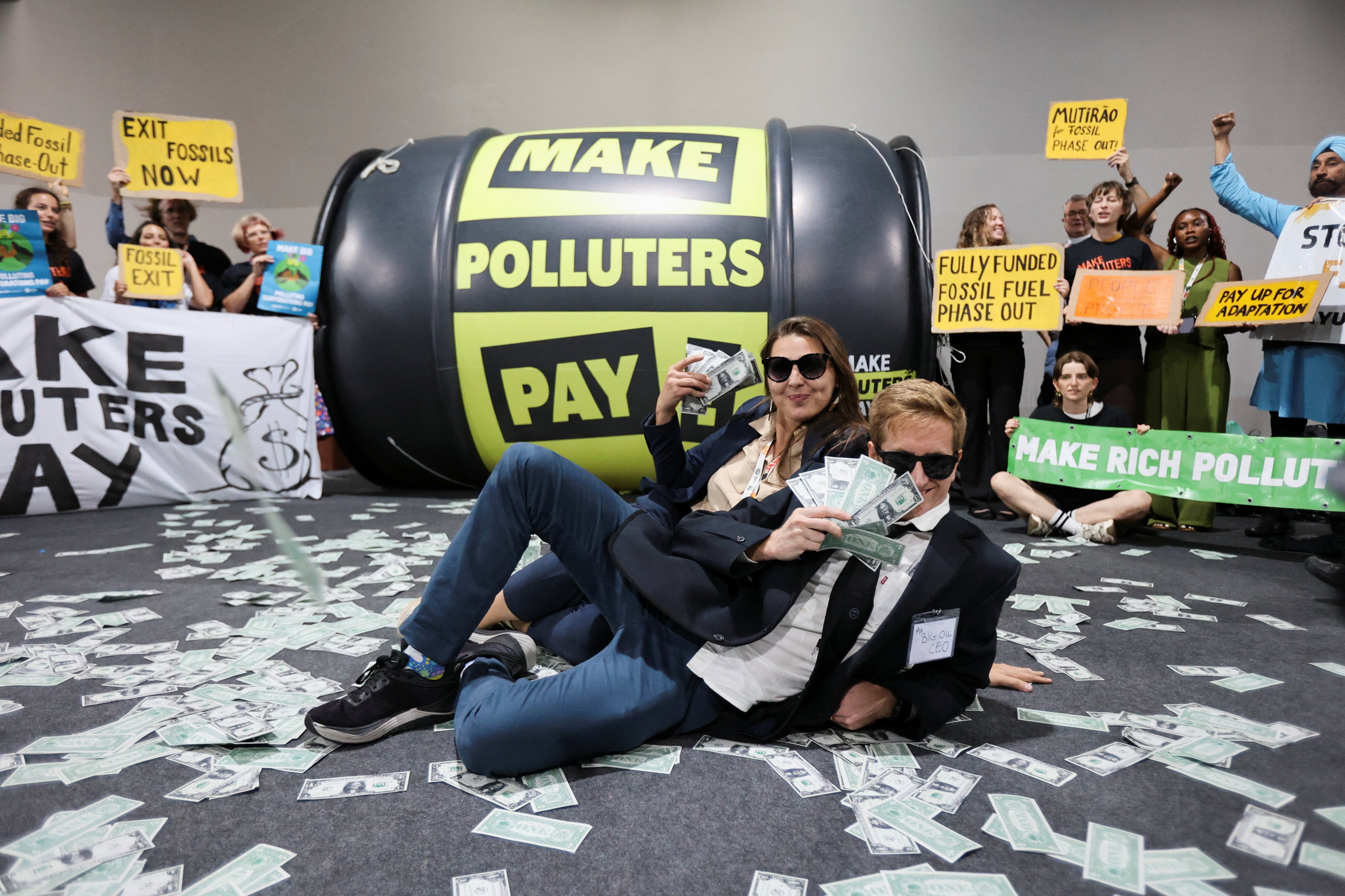 Activists from the Make Polluters Pay coalition pose with fake currency bills in front of a giant oil barrell balloon during a performance urging oil companies to fund climate solutions in Belem, Brazil, on Wednesday. Photo: Reuters