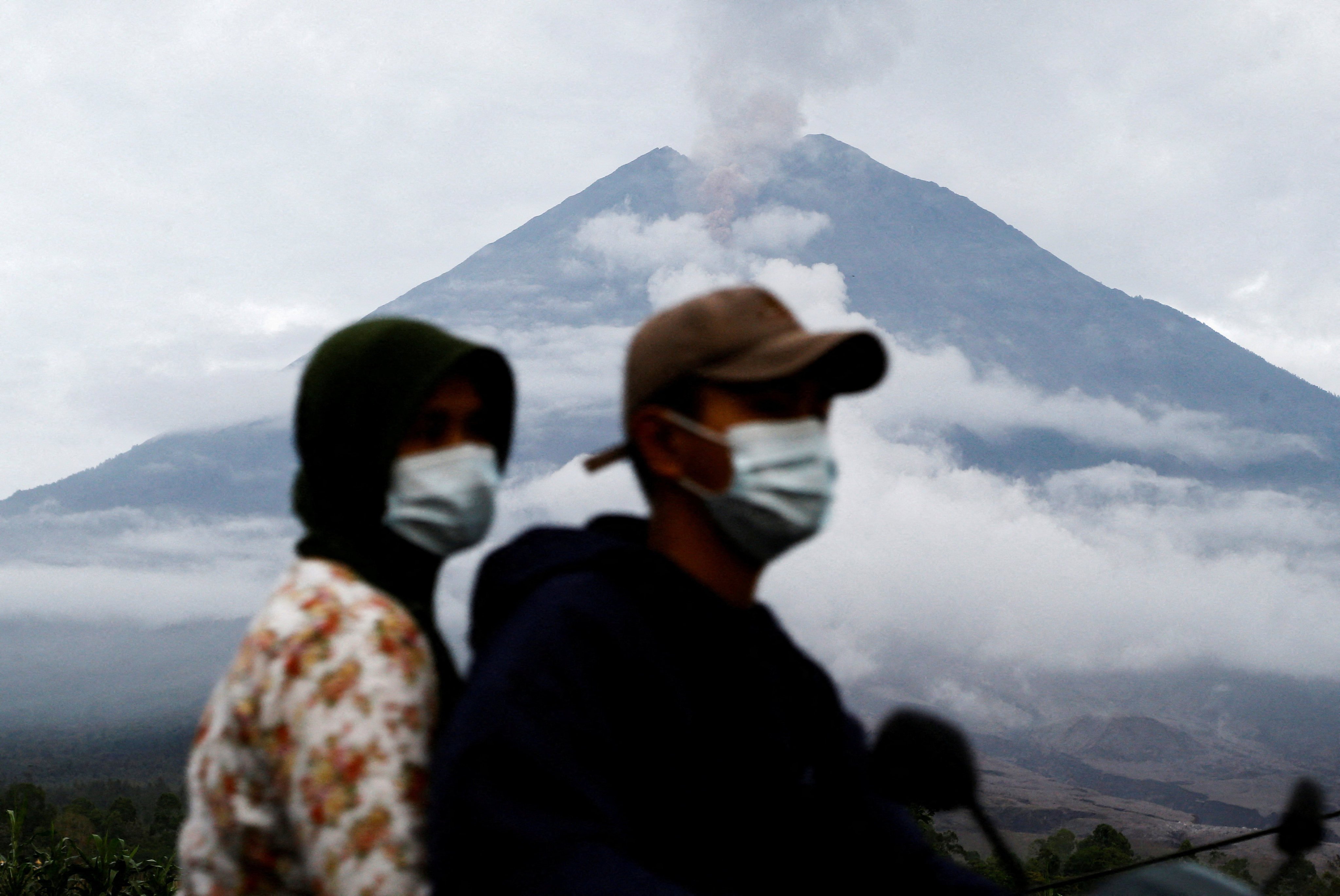 Local residents drive on a motorbike as Mount Semeru volcano spews volcanic ash during an eruption as seen in the background, in Supiturang village in Lumajang, East Java province, Indonesia, November 20, 2025. REUTERS/Dipta Wahyu     TPX IMAGES OF THE DAY