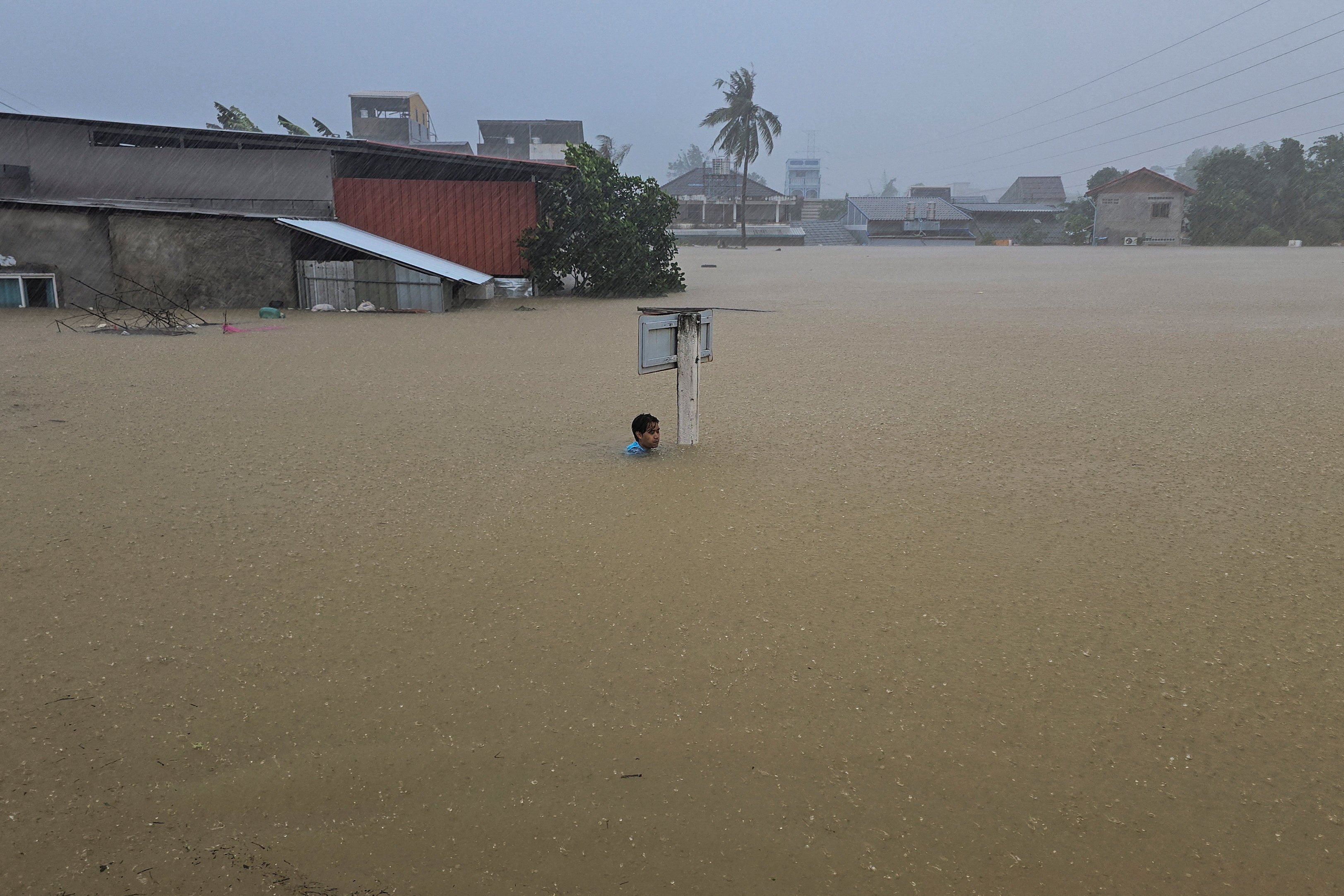 A man clings to a street sign pole in a flooded street after being swept there while going out to get food supplies in Hat Yai district on Monday. Photo: Reuters