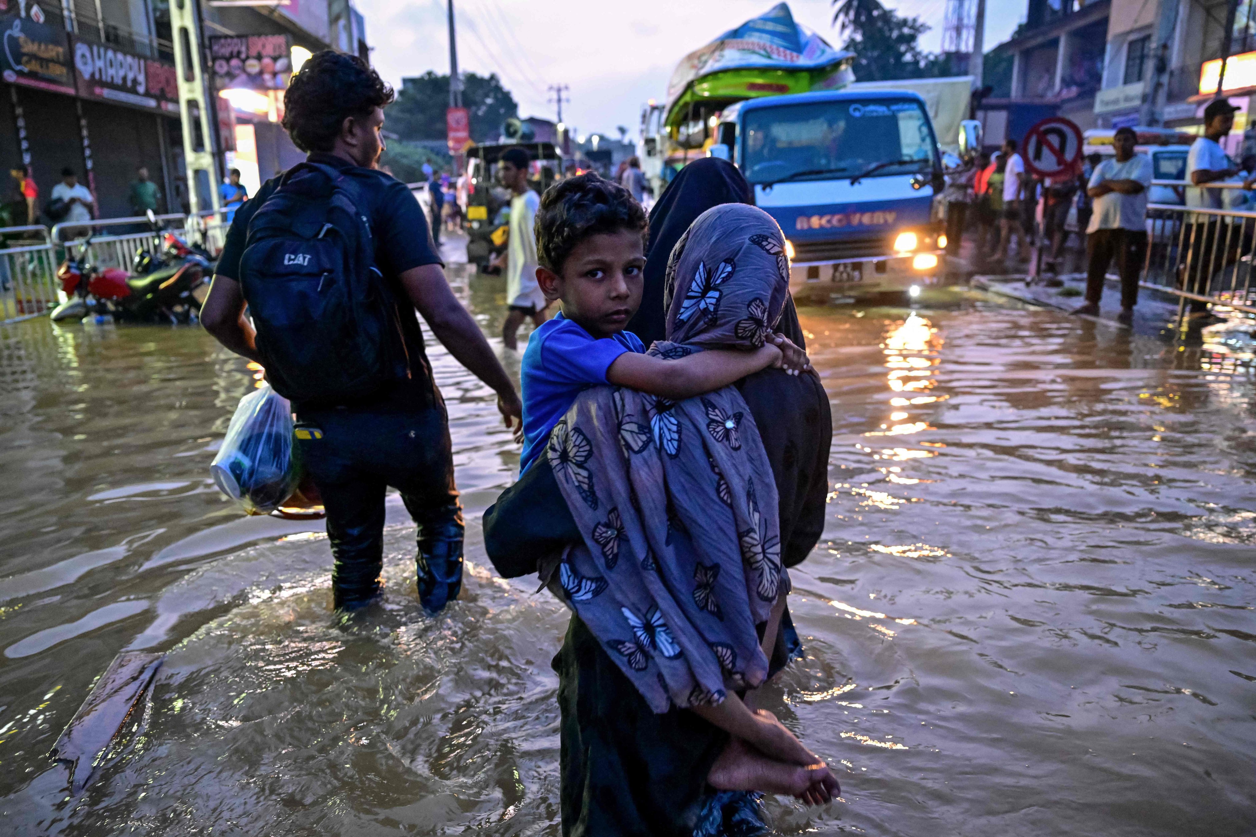 A woman carries a child as she wades through a flooded street after heavy rainfall in Wellampitiya, Sri Lanka, on November 30. Photo: AFP