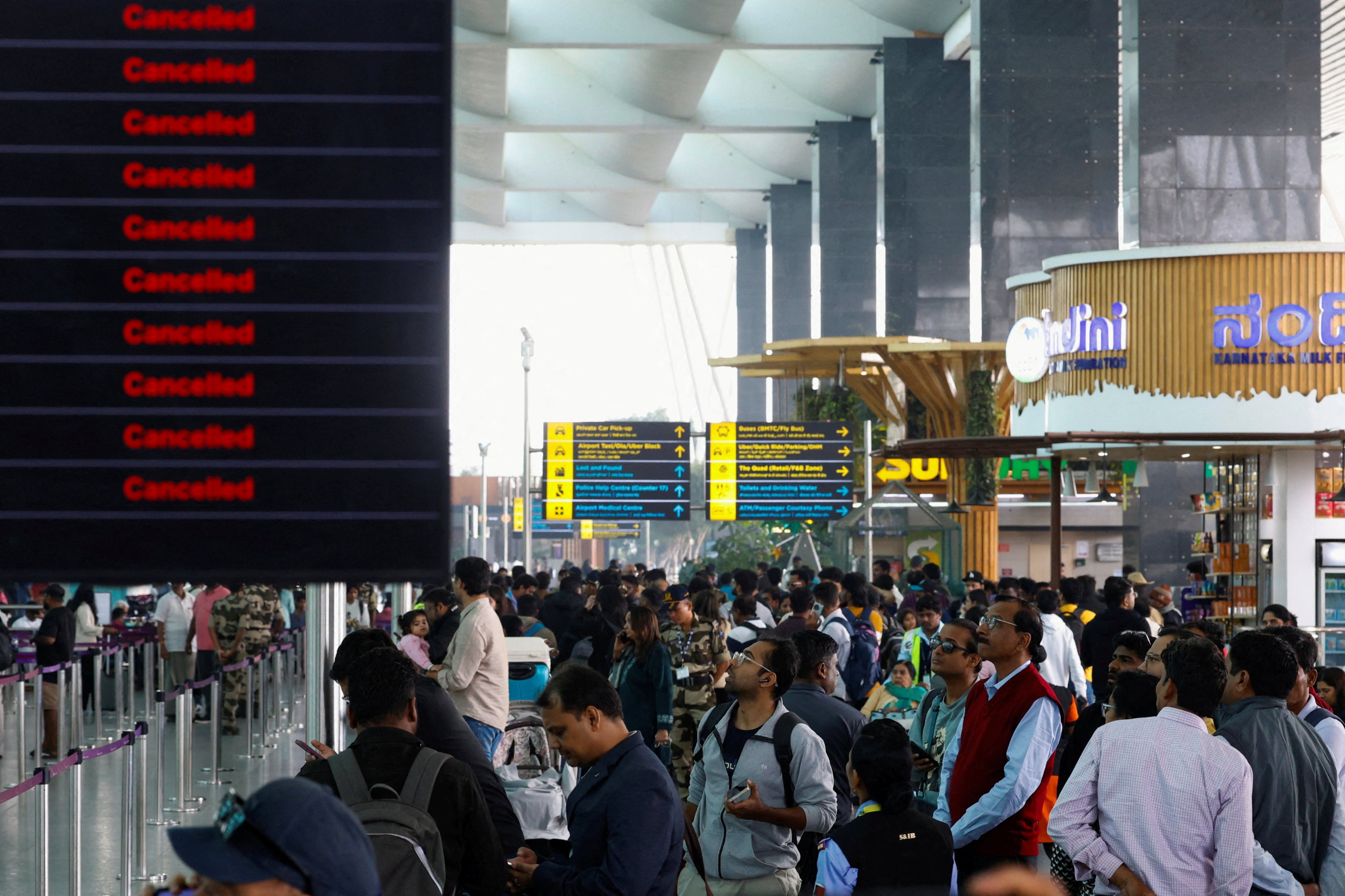 Travellers look at updates on flights, as they stand next to a screen displaying details of cancelled IndiGo airlines flights, at Kempegowda International Airport in Bengaluru, India, on Saturday. Photo: Reuters