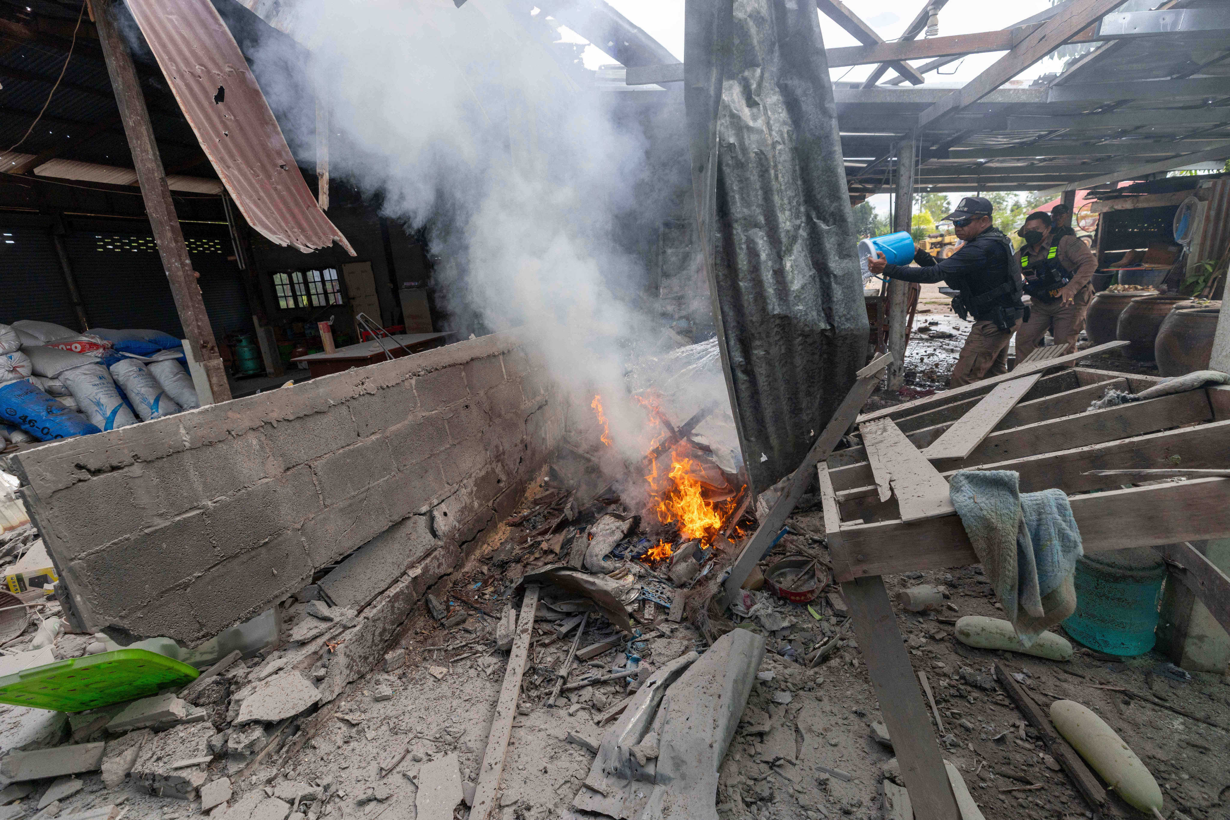 A Thai police officer splashes water to control a fire at a house which was reportedly damaged by a Cambodian artillery strike in Thailand’s Surin province on Thursday. Photo: AP