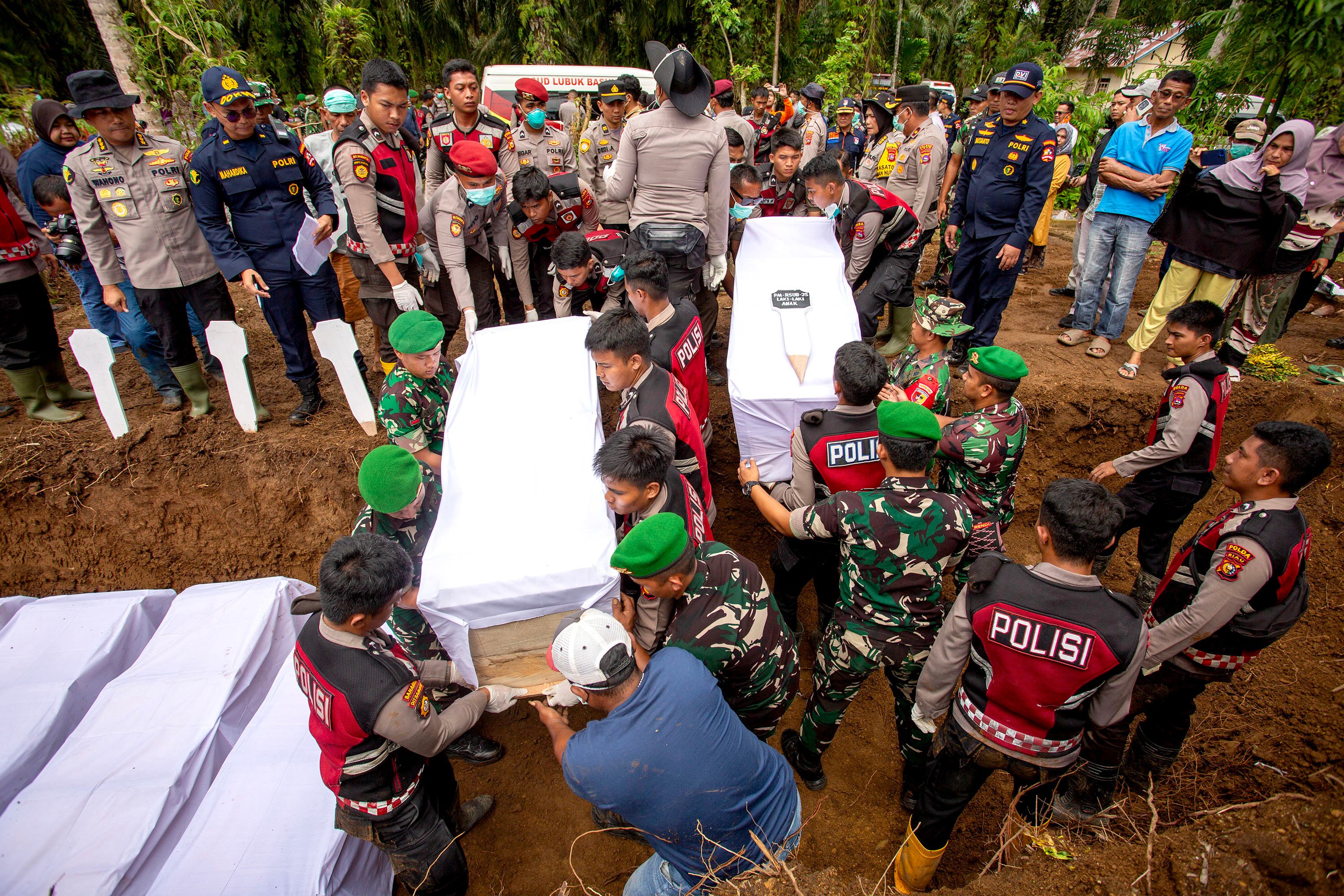 Police officers help to carry coffins on Thursday during a mass burial for victims of floods and landslides in West Sumatra, Indonesia. Photo: Xinhua