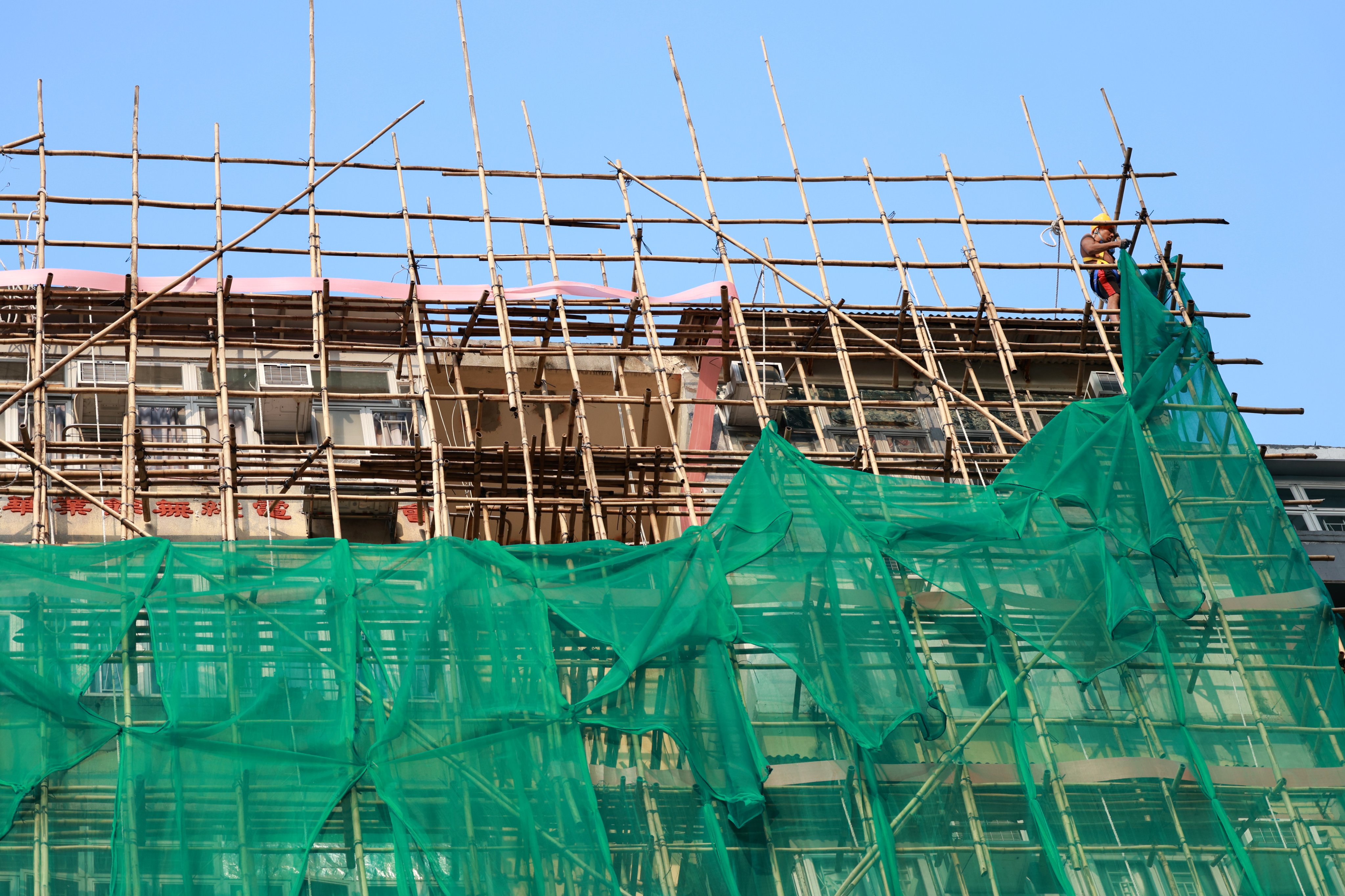 A worker removes netting from a scaffold in Hong Kong on December 5, following the deadly fire at Wang Fuk Court in Tai Po. Photo: EPA