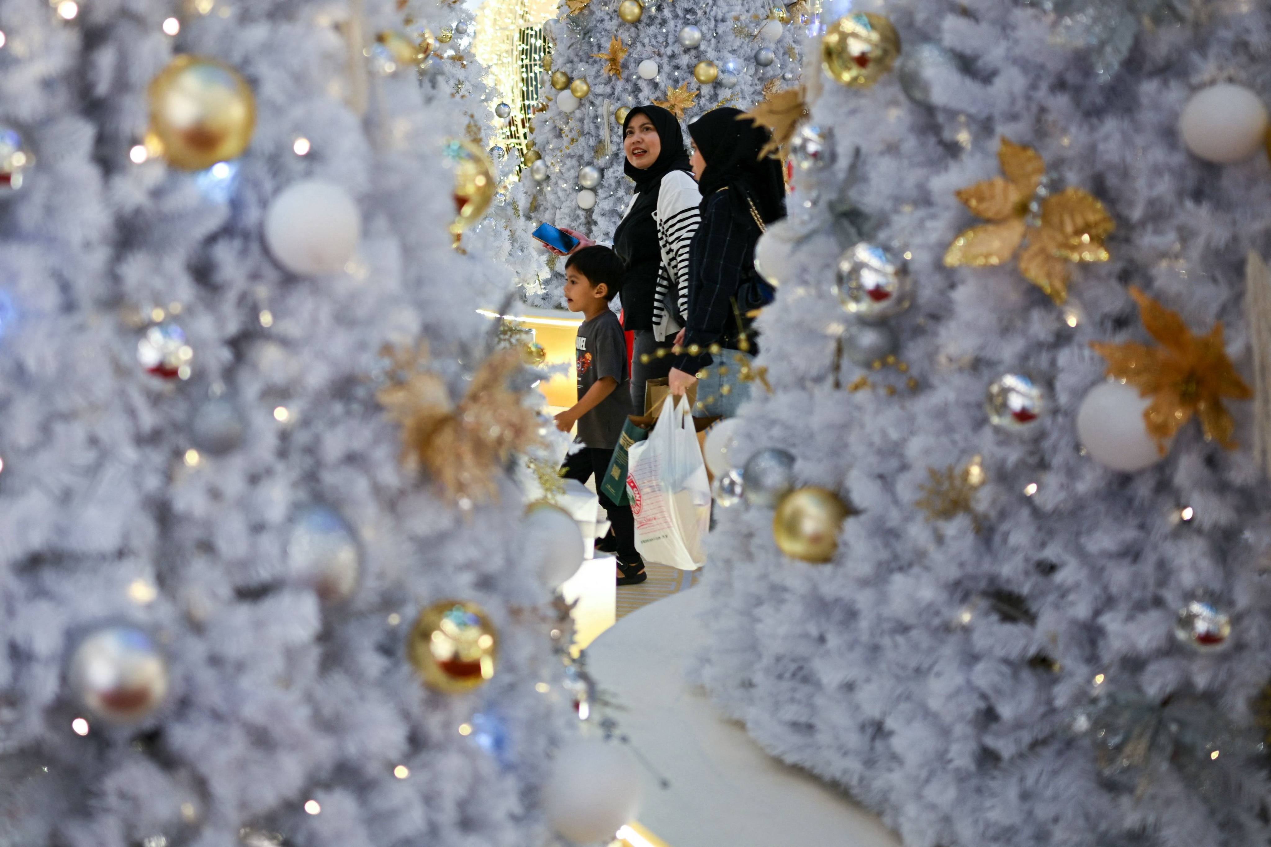 Shoppers walk around Christmas trees at a mall in Kuala Lumpur on Friday. Photo: AFP
