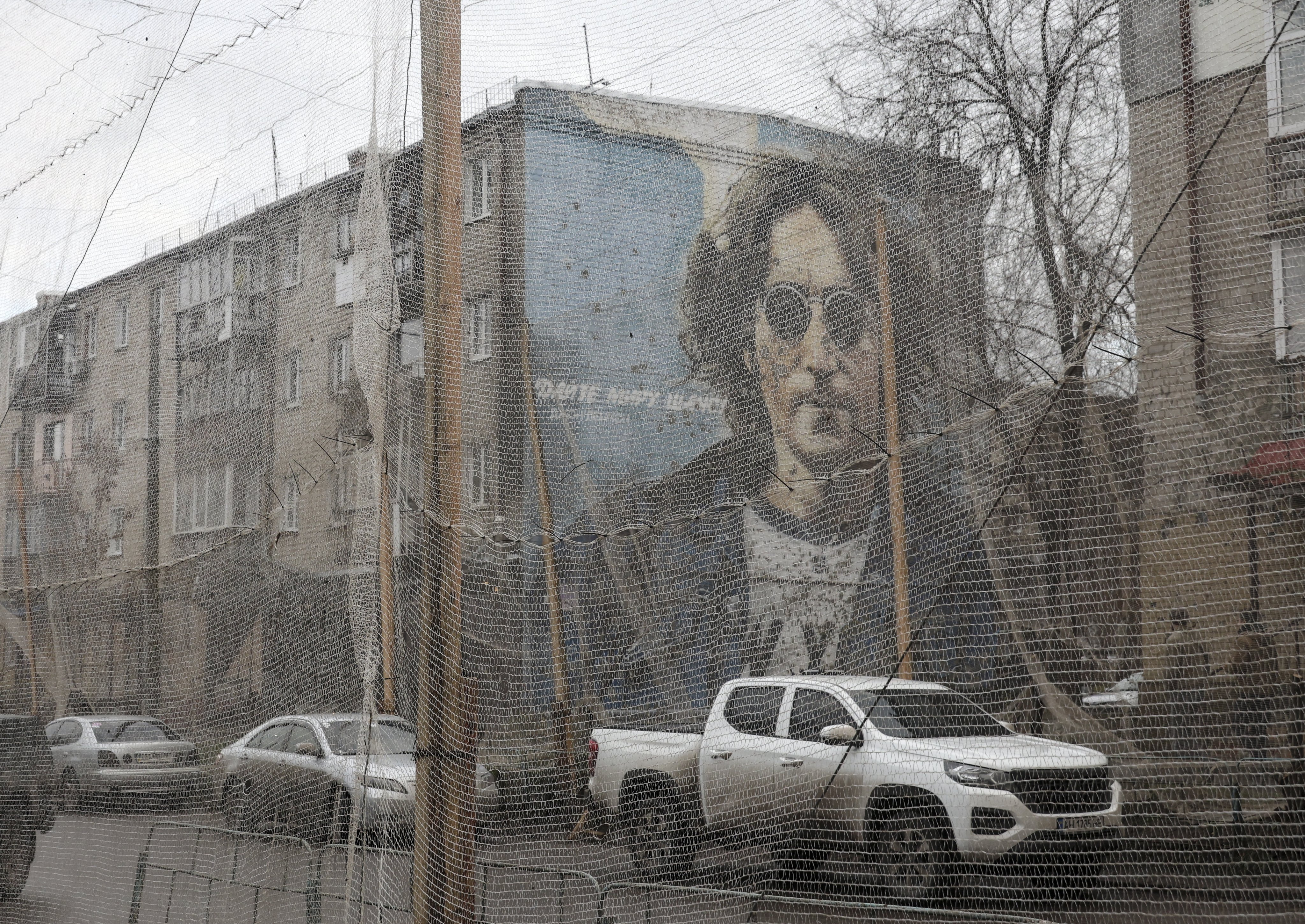 A “Give peace a chance” mural depicting musician John Lennon overlooks anti-drone nets along a road in the city of Izyum in Ukraine on December 12. Photo: EPA