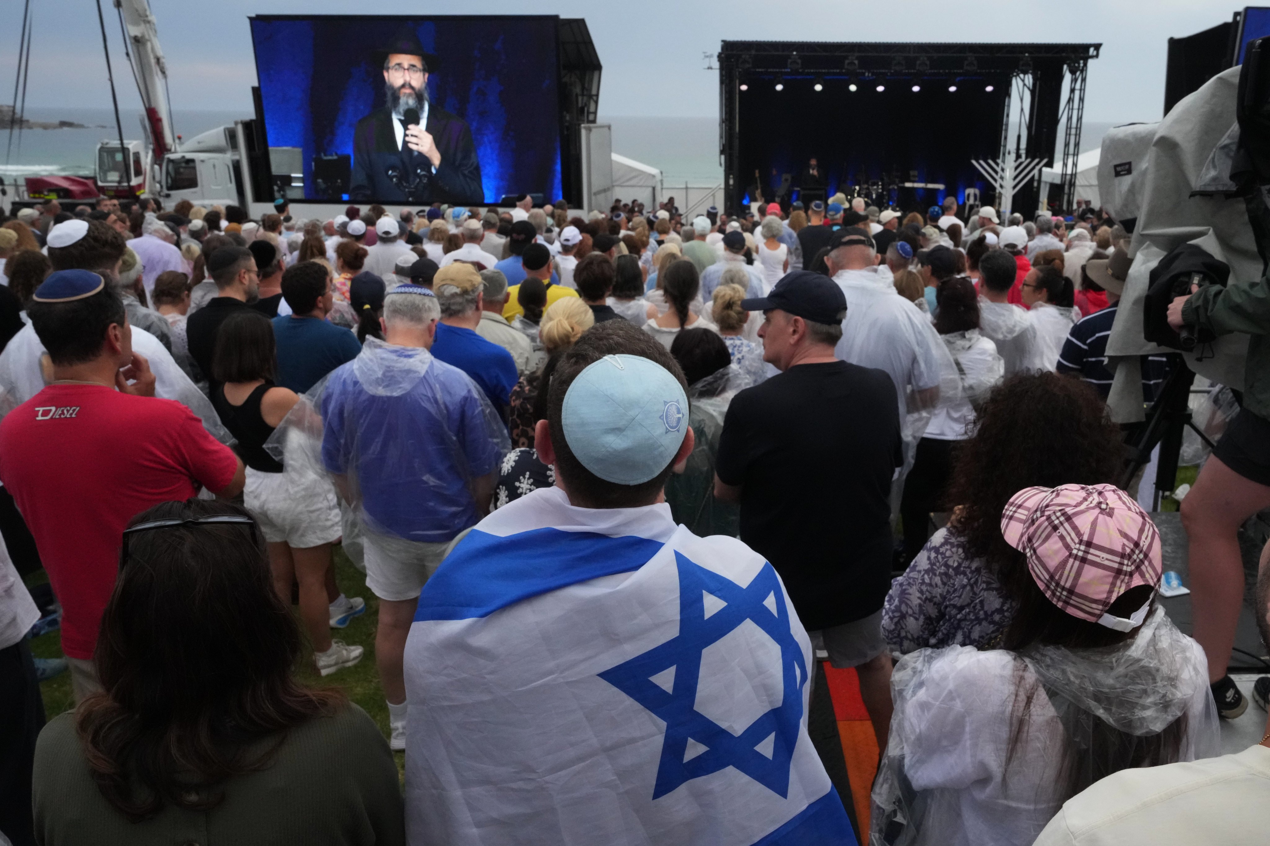 A person with Israel’s flag and other people attend a ceremony to mark the National Day of Reflection for victims and survivors, at Bondi Beach in Sydney on Sunday. Photo: AP