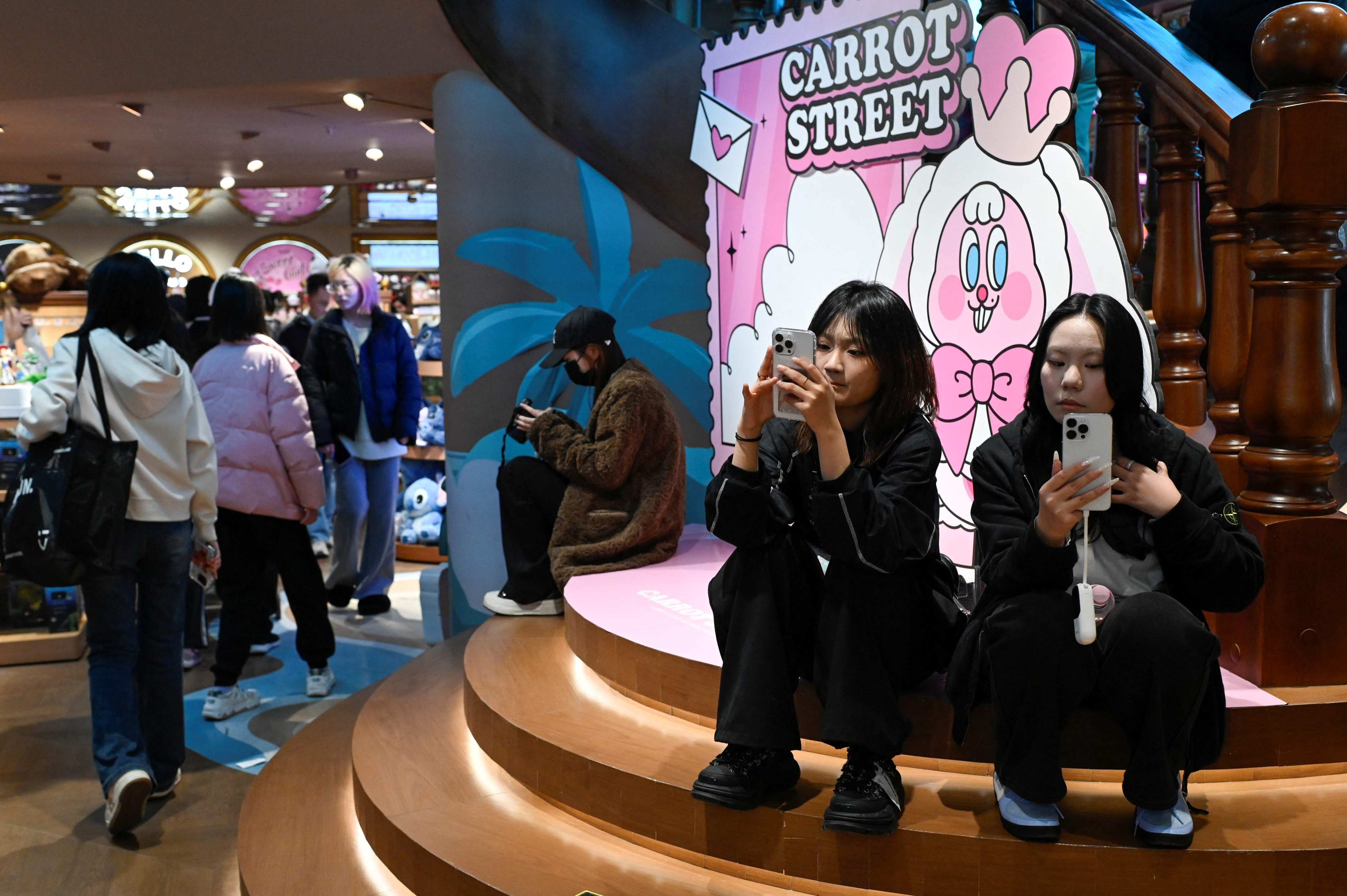 Two women use their mobile phones at a store in Beijing on November 29, 2025. Photo: AFP