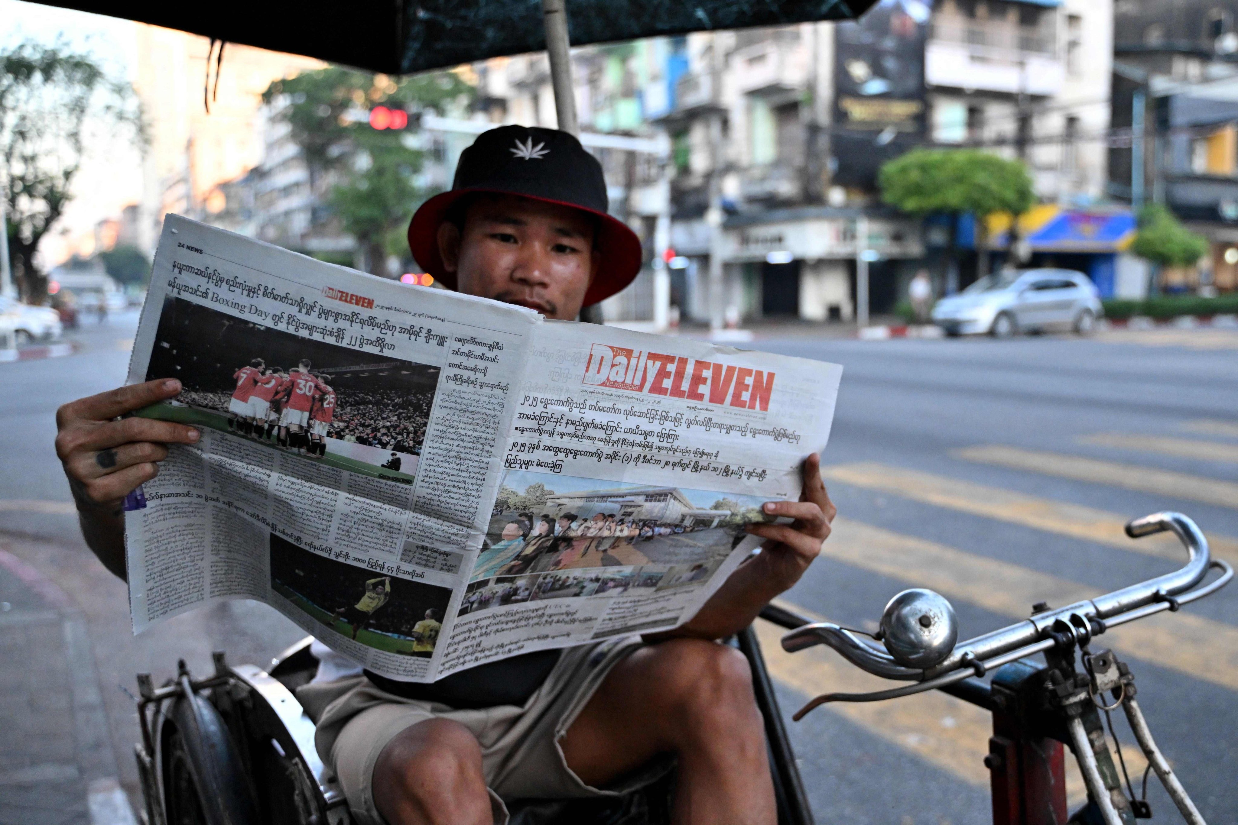 A trishaw driver sits and reads a newspaper reporting on Myanmar's general election in Yangon on December 29, 2025. Photo: AFP