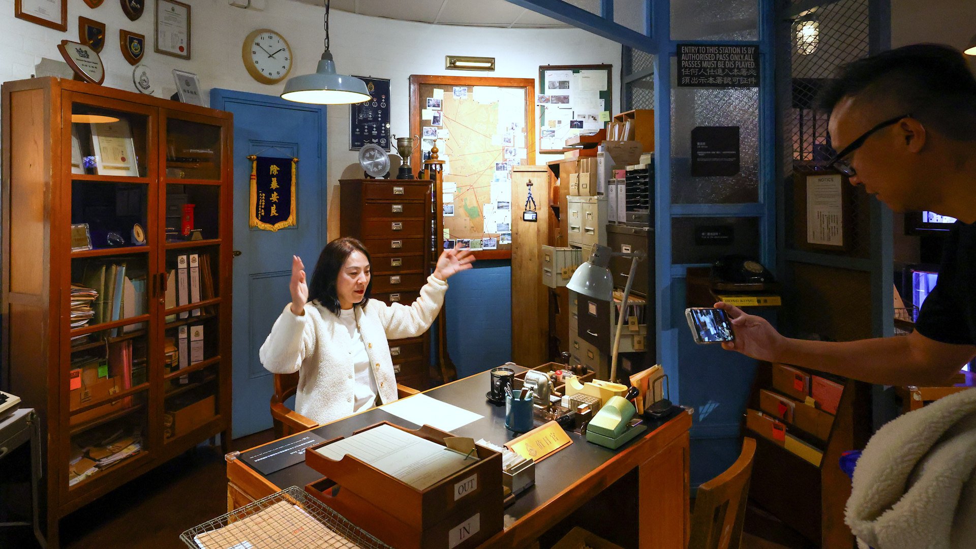 First day of “Yau Ma Tei Police Station: A Cinematic Journey” exhibition, presented by the Cultural and Creative Industries Development Agency under the Culture, Sports and Tourism Bureau,

C.I.D. Office-Inspired by police stations of the 1970s and 1980s, the exhibition recreates an imagined C.I.D. Office featuring an office, surveillance room, armoury, exhibit office and identification parade room. Traces and clues drawn from classic police and crime films are embedded throughout the space for visitors to explore. Specially designed sound and lighting effects further enhance the cinematic atmosphere, transforming the C.I.D. Office into a highly immersive and photo-friendly setting.