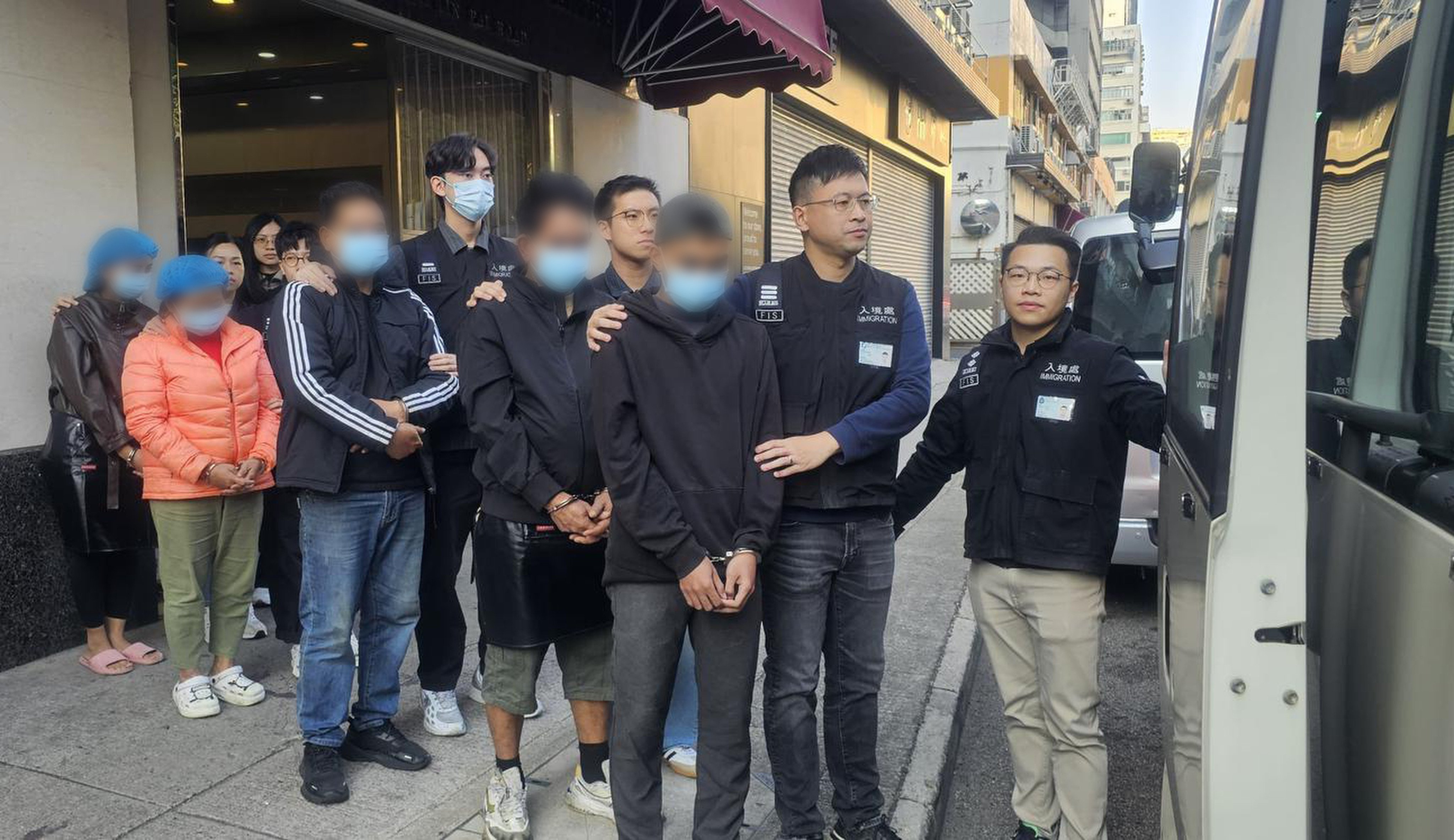 Hong Kong immigration officers escort the arrested suspects to a van after searching the food factory in Kwai Chung on Saturday. Photo: Handout