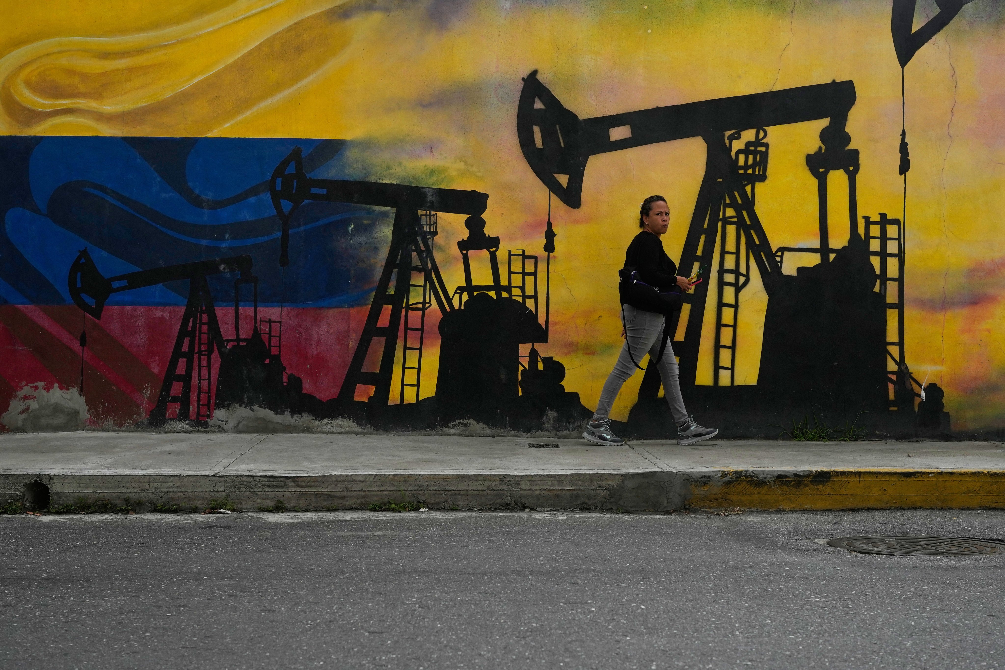 A local walks past a mural featuring oil pumps and wells in Caracas, Venezuela, on Tuesday. Photo: AP