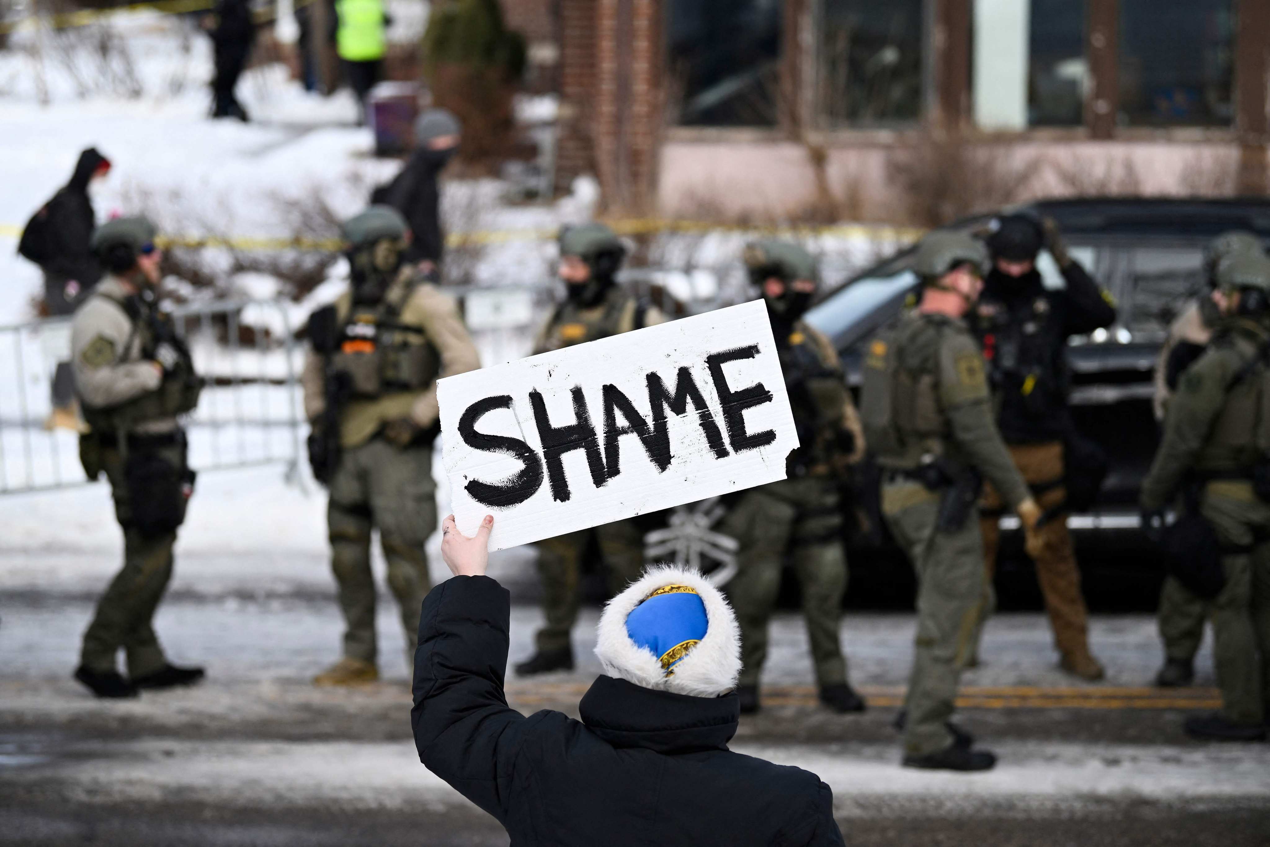 A protester holds a sign that reads “Shame” as members of law enforcement work the scene following a shooting by an ICE agent in Minneapolis, Minnesota, on Wednesday. Photo: AFP