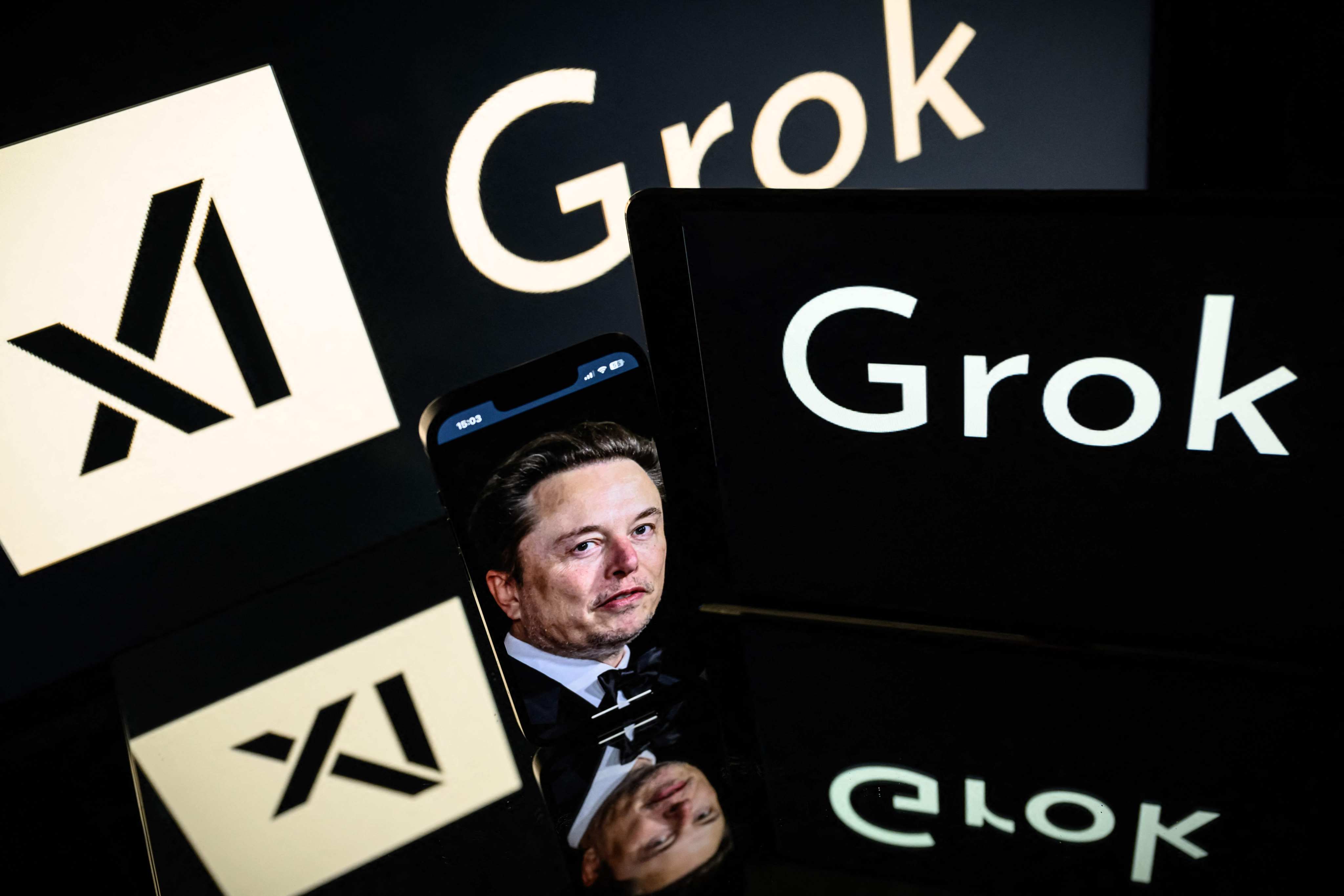Screens display the logo of Grok, a generative artificial intelligence chatbot developed by xAI, and its founder Elon Musk. Photo: AFP
