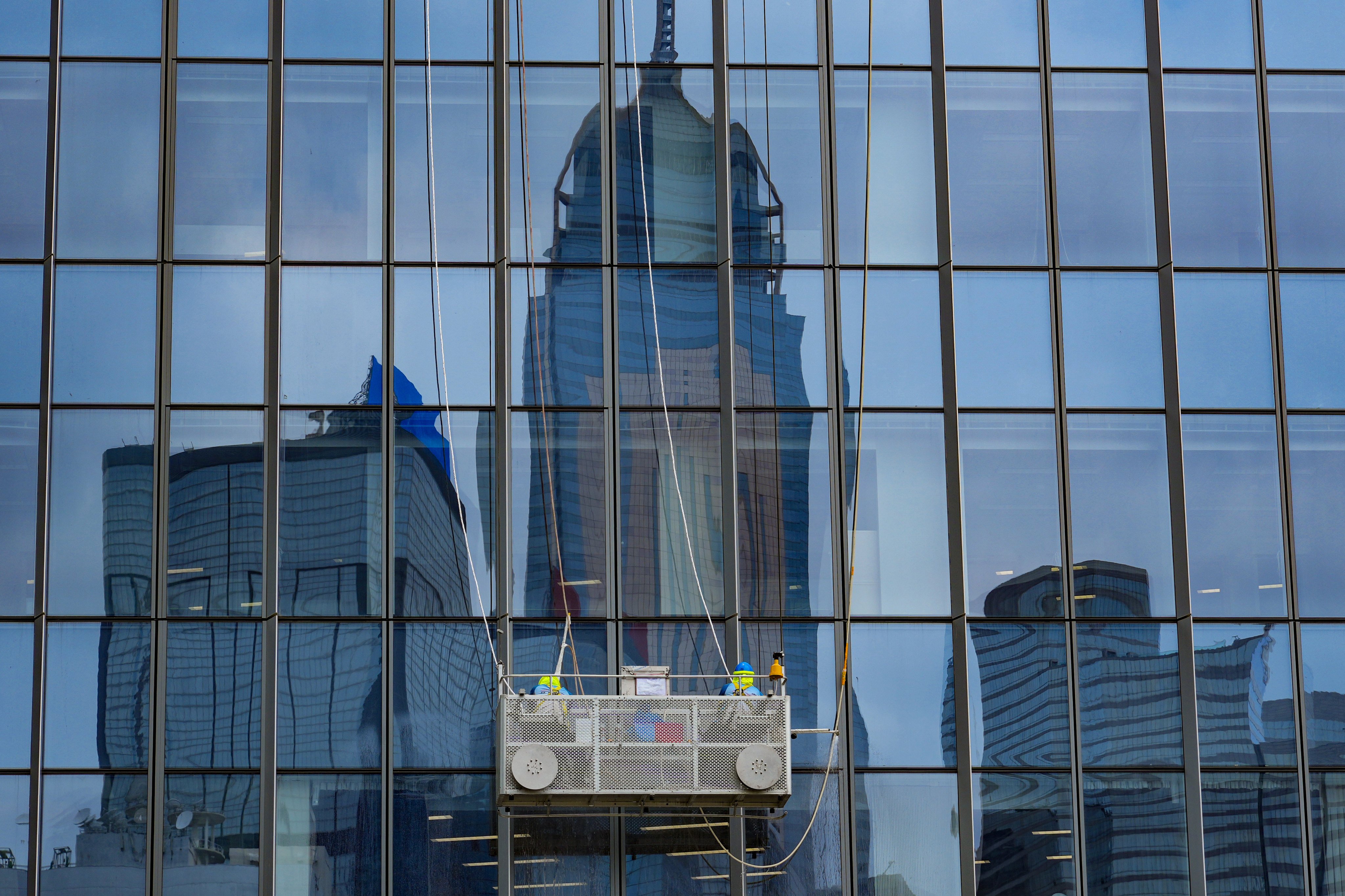 Workers clean the windows of a building in Tamar, with reflections of Wan Chai office towers reflected in the glass, on April 30, 2025. Photo: May Tse